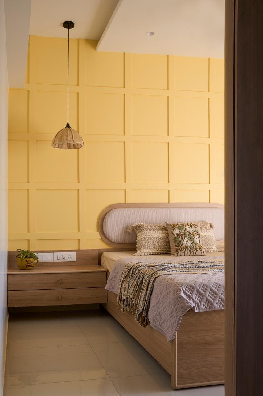 The bedroom, where a sunshine-yellow panelled wall meets an oval upholstered headboard beneath a rattan pendant