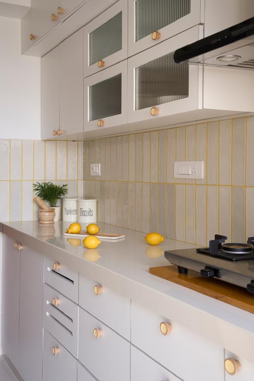 The kitchen, where a pale tile field with mustard-yellow grout lifts a restrained white galley into something quietly joyful