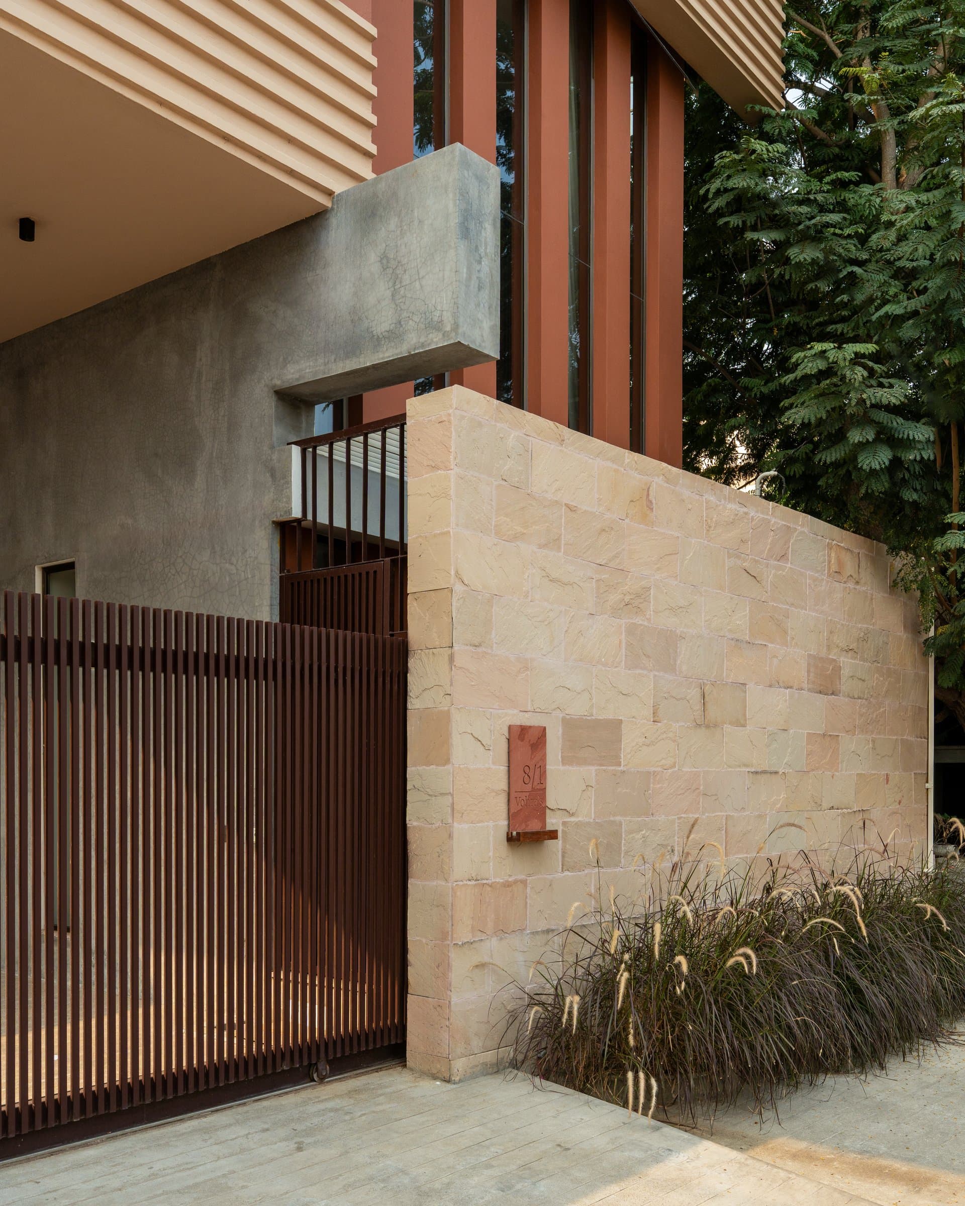 The entry gate, where slatted bronze meets a warm sandstone wall to introduce the home's material register