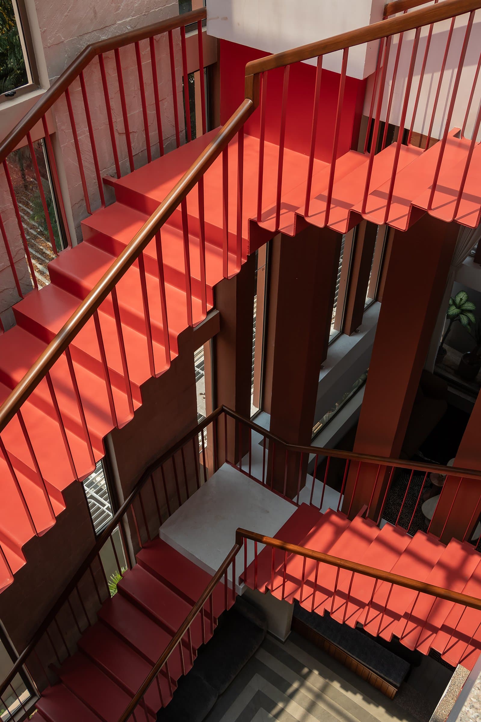 The staircase seen from above, its saturated red treads unfolding through the volume against a warm wooden handrail