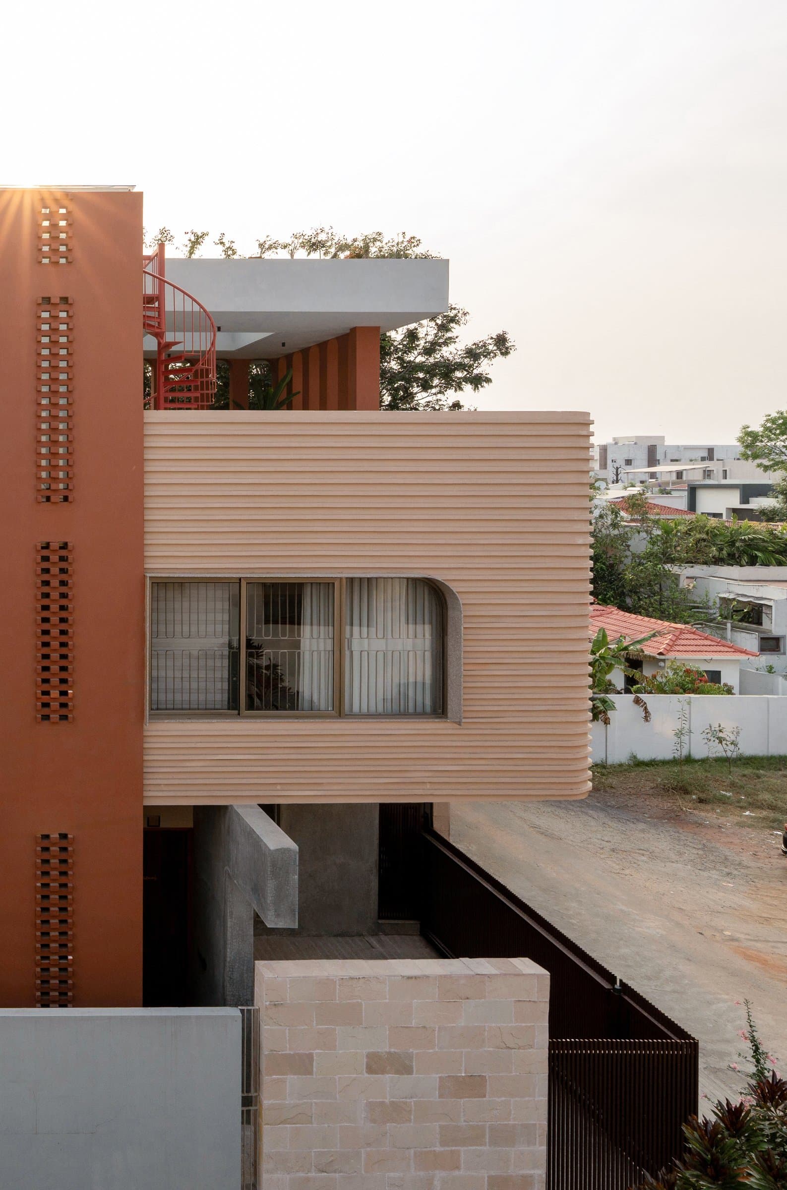 A raised view of the upper volumes, revealing the ribbed cantilever, terracotta fins, and the coral spiral stair on the terrace