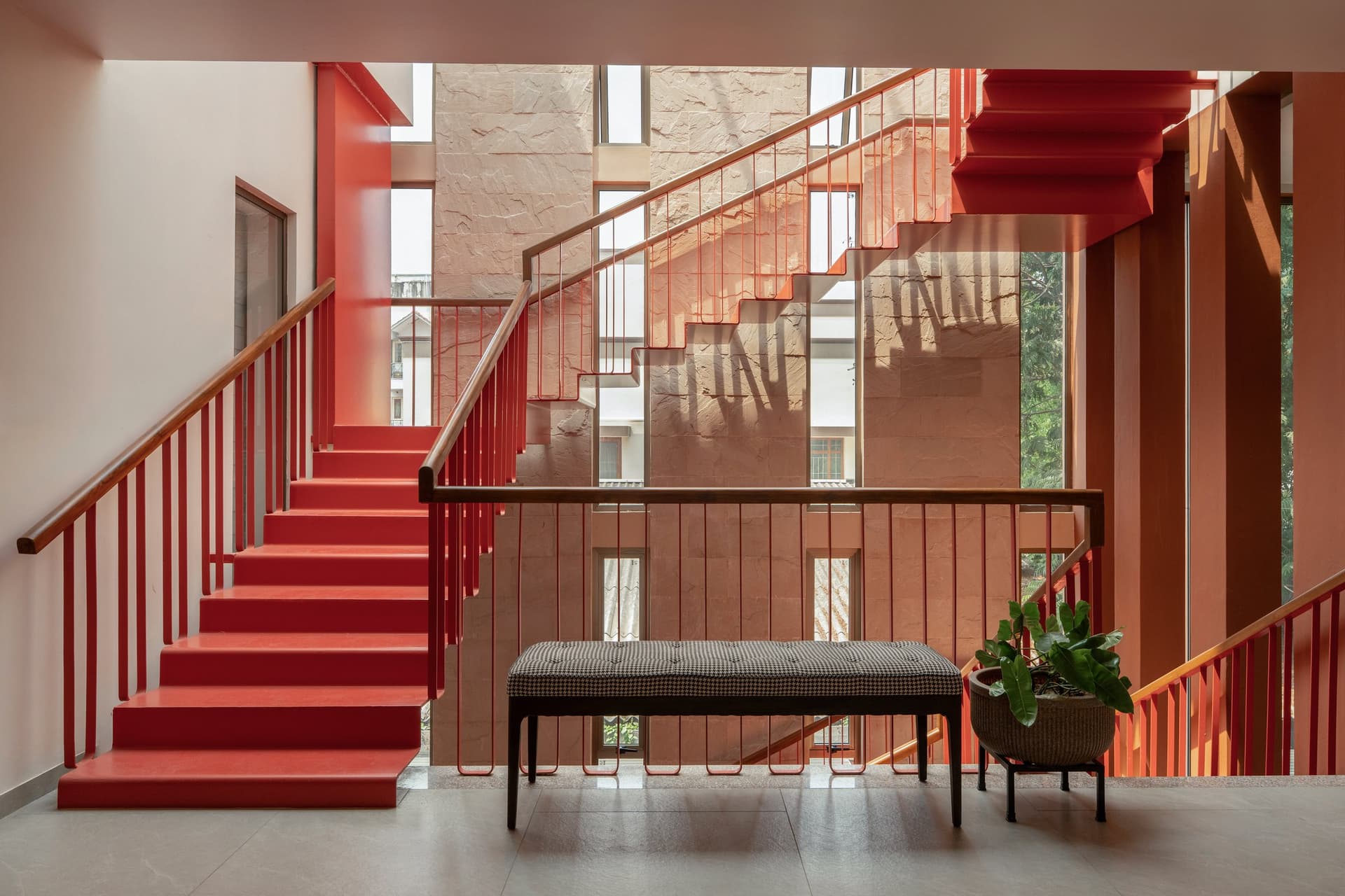 The stair hall, where a terracotta balustrade meets warm sandstone cladding and a landing bench introduces a moment of pause