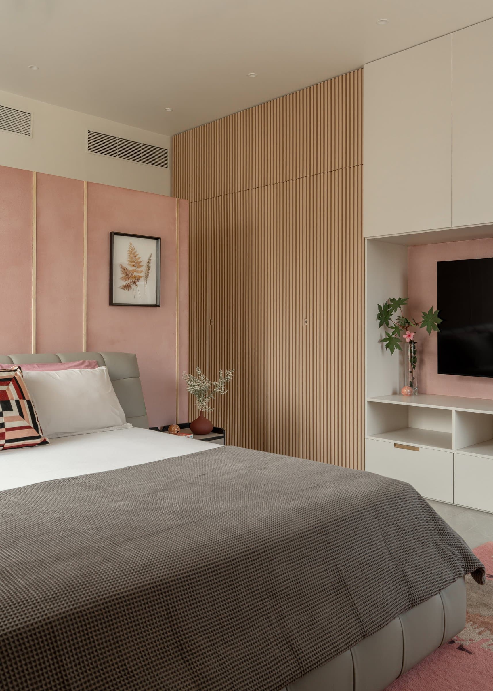 The primary bedroom, where a dusty-pink upholstered wall meets a full-height run of slatted oak joinery
