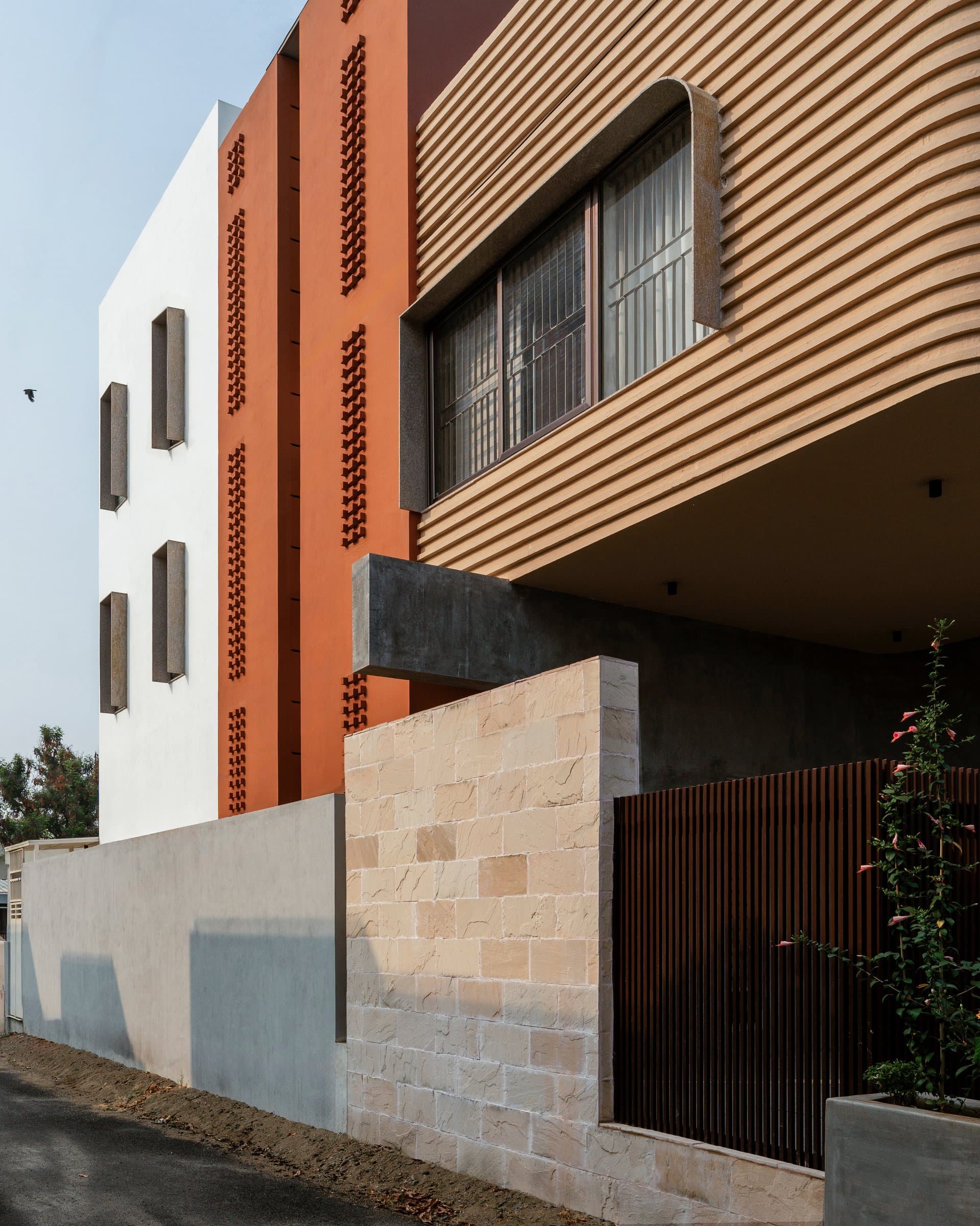 The side elevation, where white shadow-box windows, an ochre jaali, and the ribbed cantilever meet as three distinct architectural planes