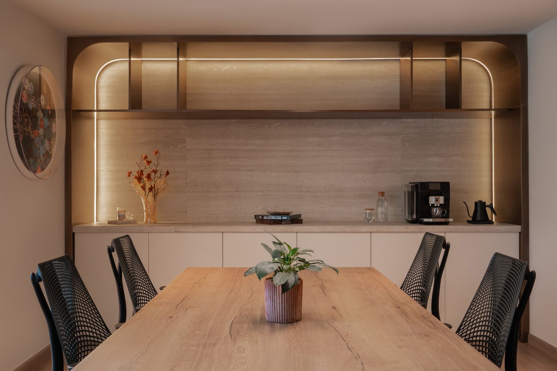 The coffee counter, set within a warm-metal arch, translates a residential sideboard into workplace vocabulary