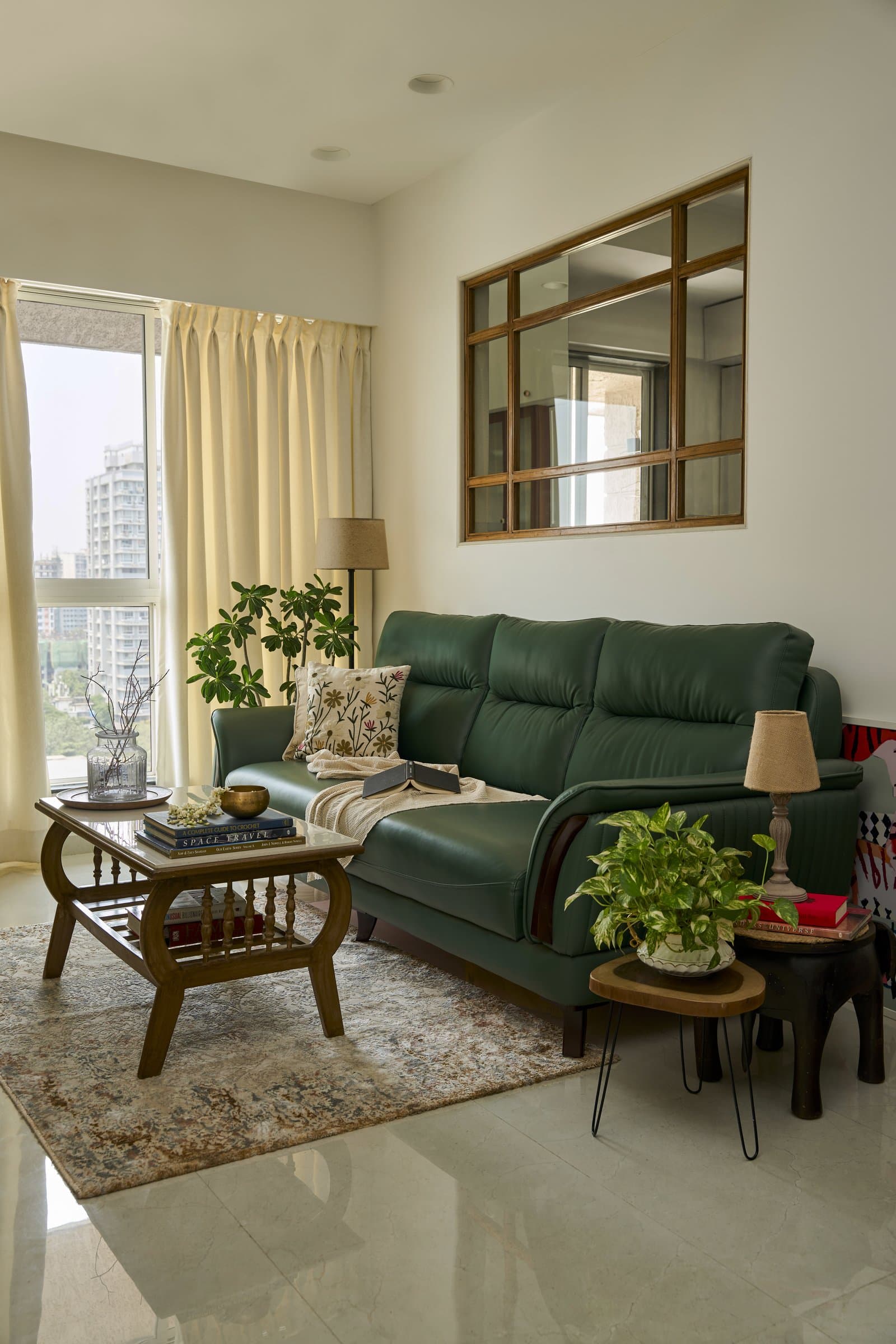 The living room, where a deep green leather sofa and a wooden framed internal window borrow light and sightlines from the adjacent space