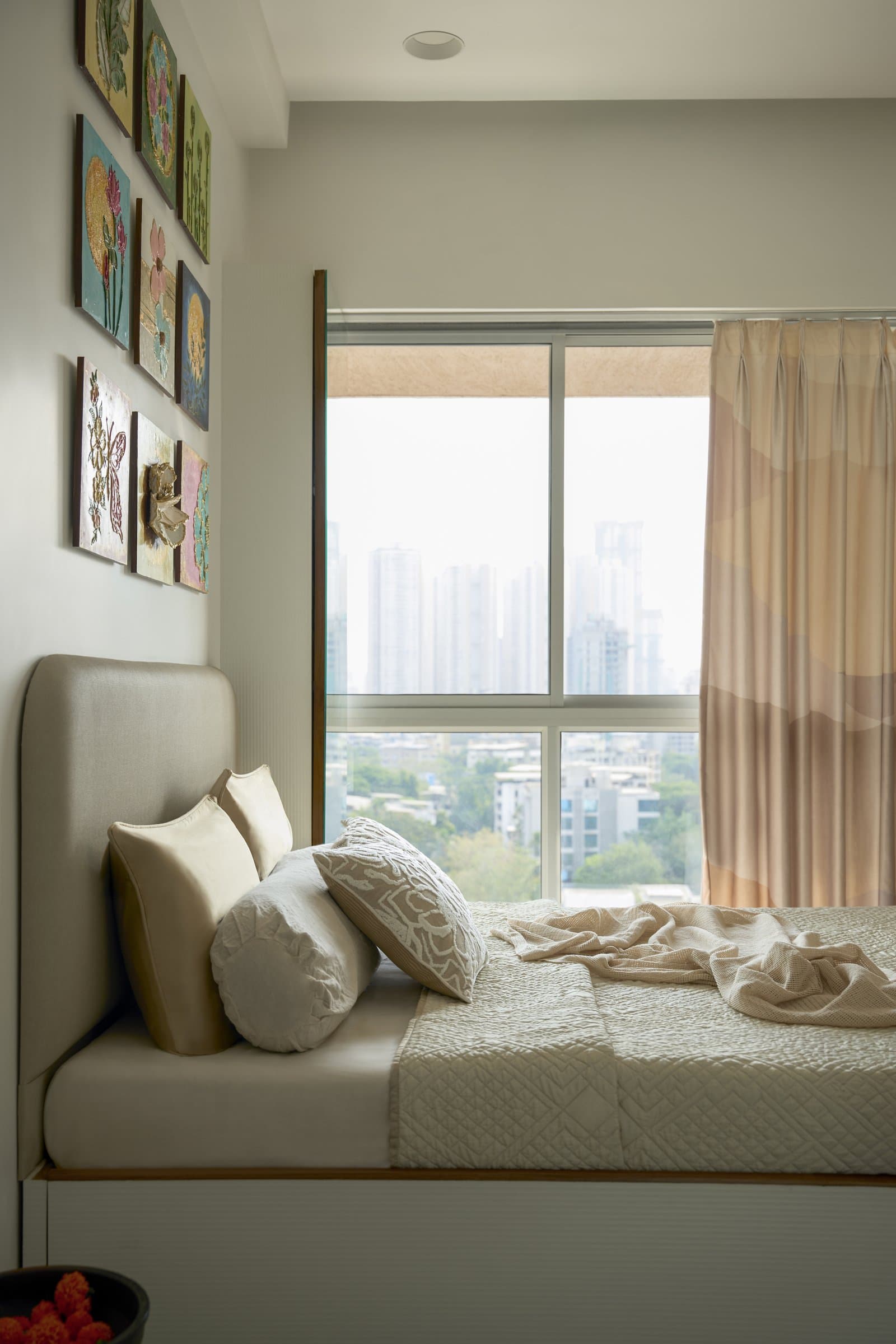 The low bed oriented to the window, softened by peach ombre drapery and cushions in cream and beige
