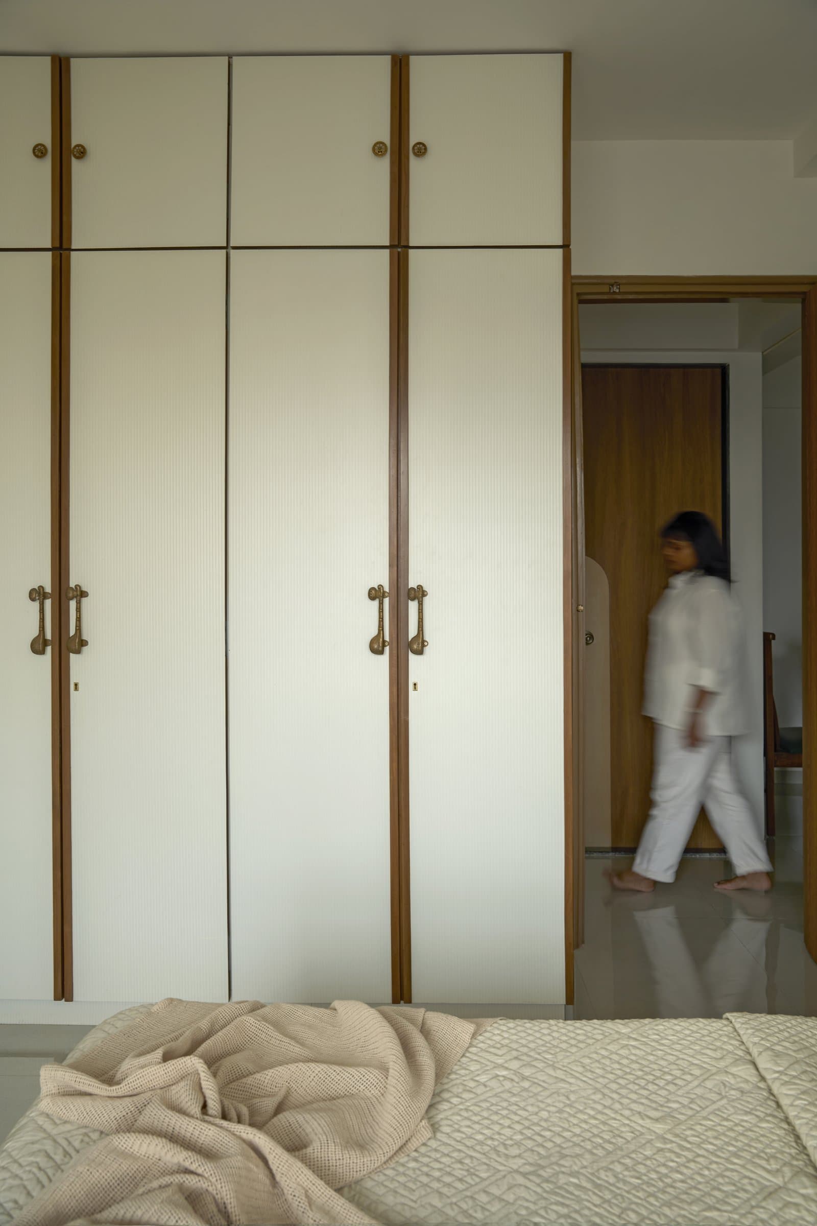 The bedroom cabinetry, finished in a subtly ribbed cream front with slim vertical inlays and antique brass pull handles