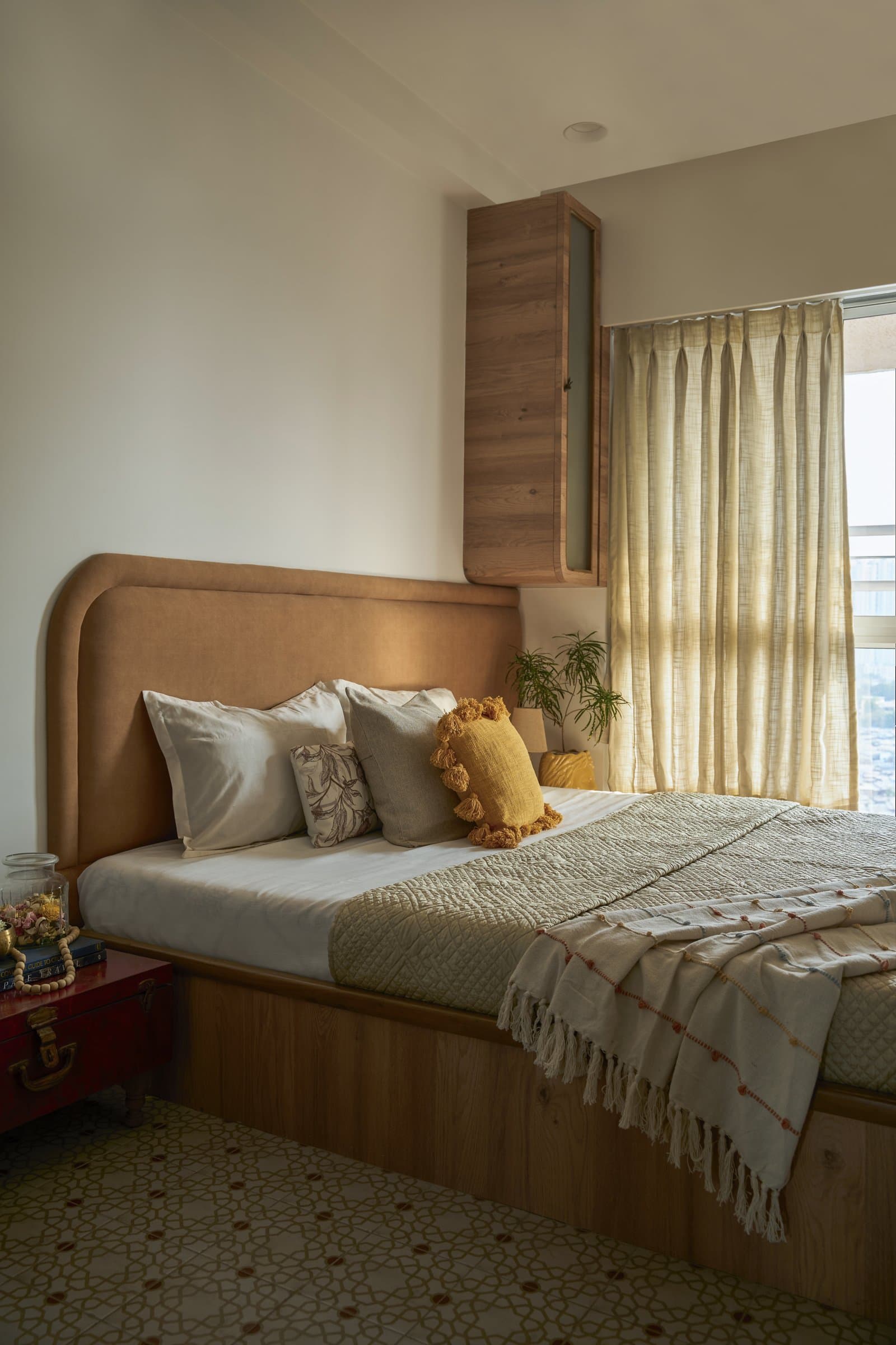 The primary bedroom, where a curved caramel upholstered headboard sits against warm walls above a patterned geometric floor