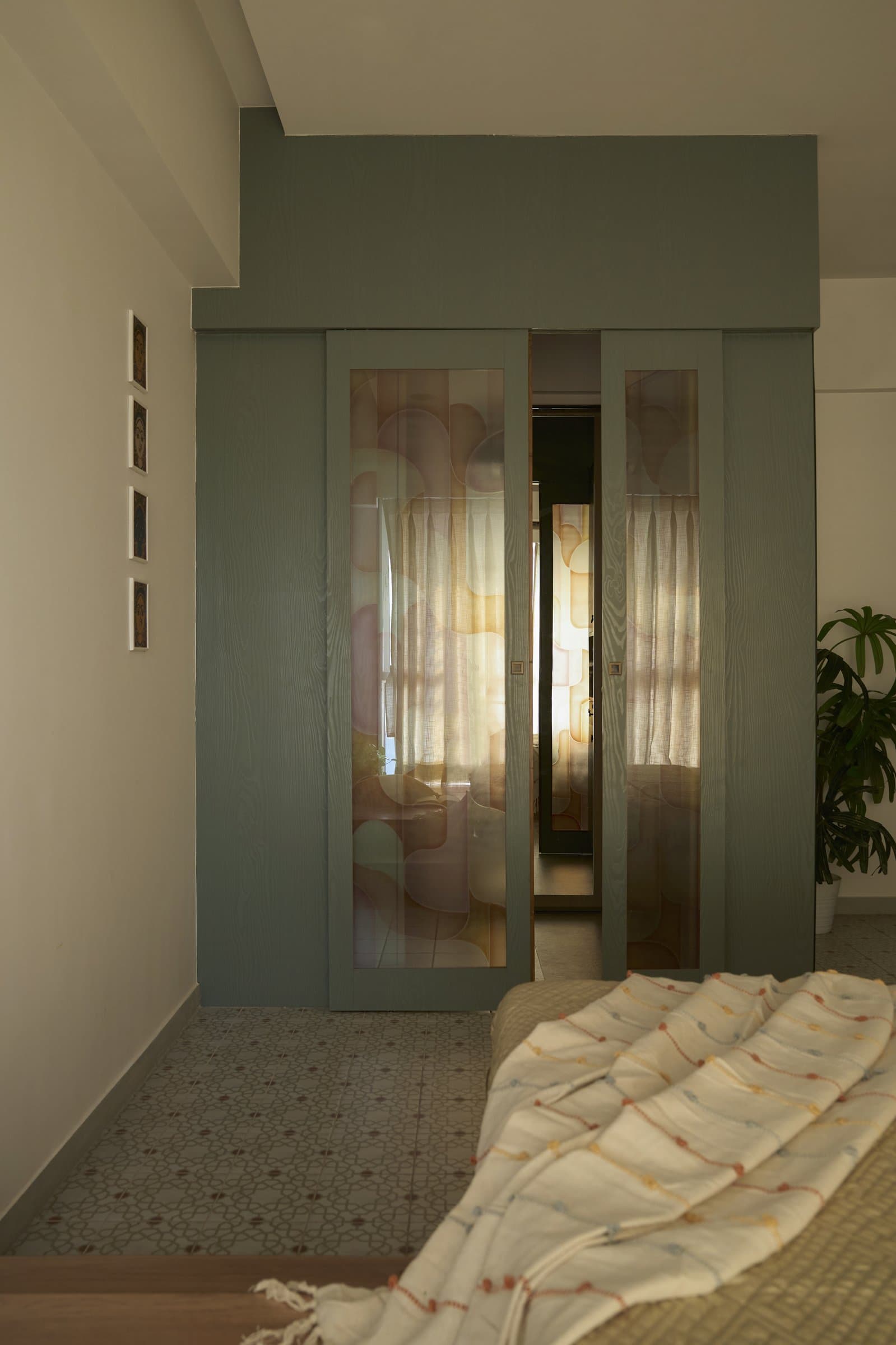 A sage green sliding partition with translucent patterned panels filters light between spaces while preserving privacy