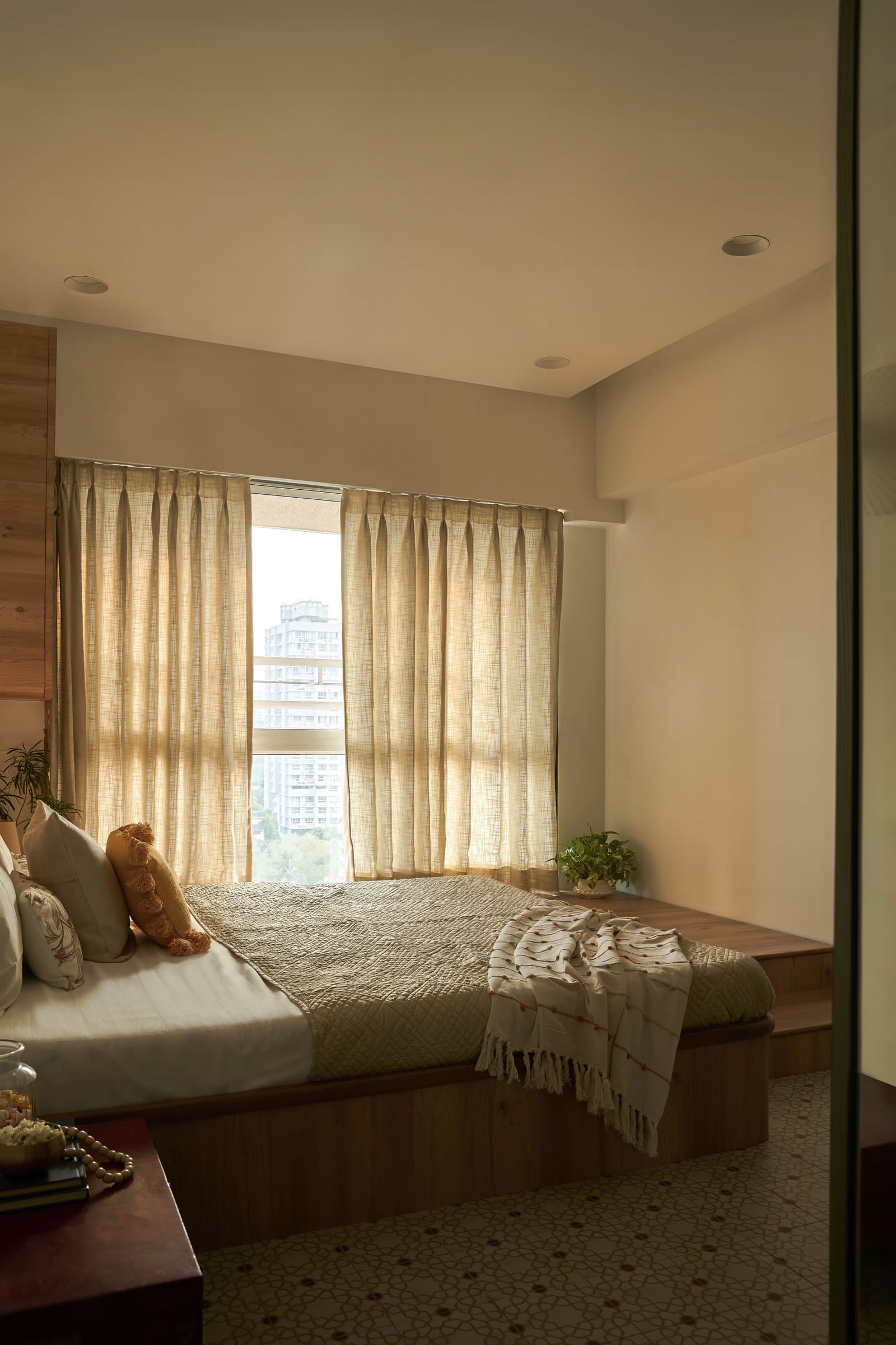 The bed extends into a raised timber platform running to the window, doubling as a low seat and a plinth for greenery