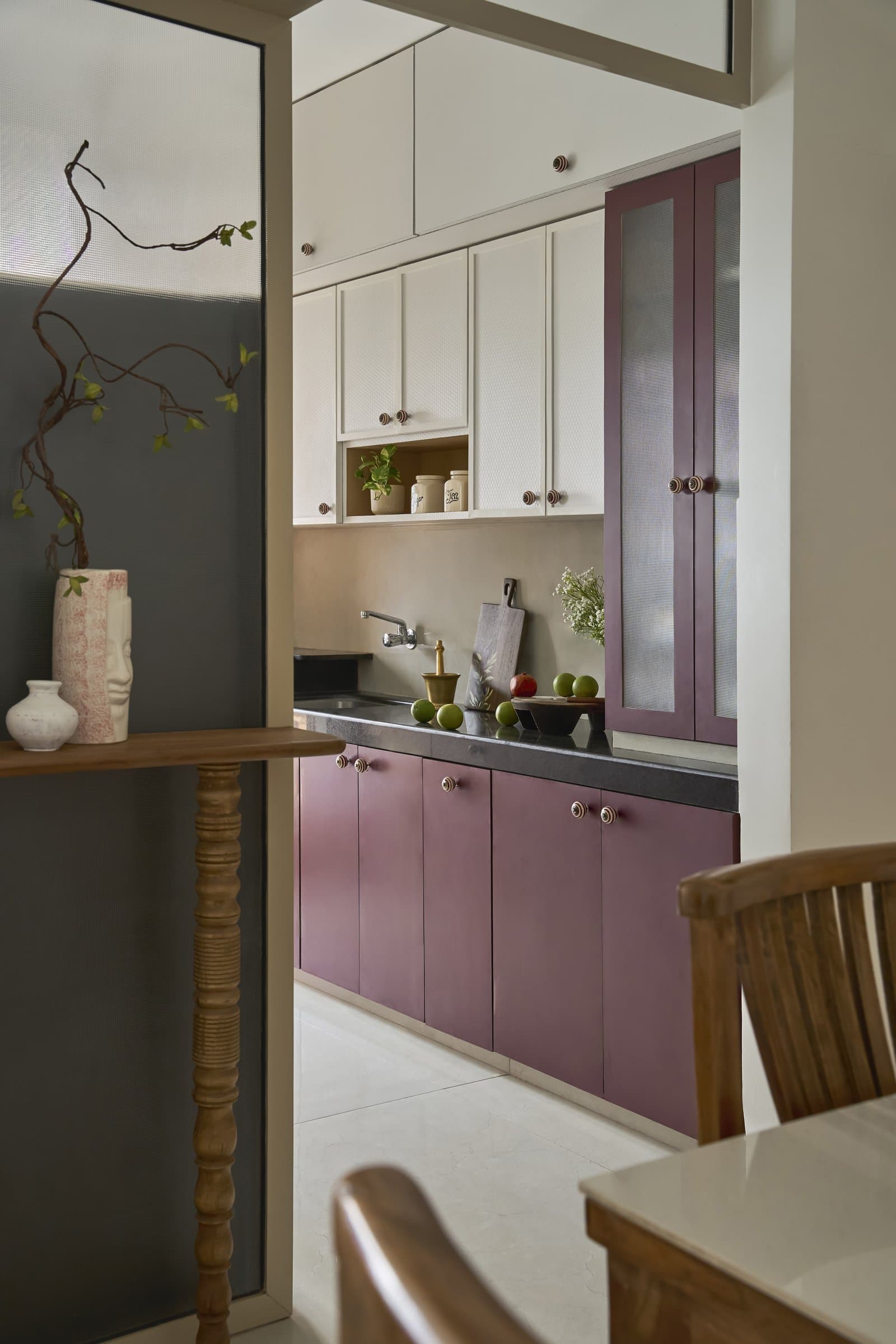 The galley kitchen, where muted plum cabinetry meets soft cream uppers and a dark stone counter