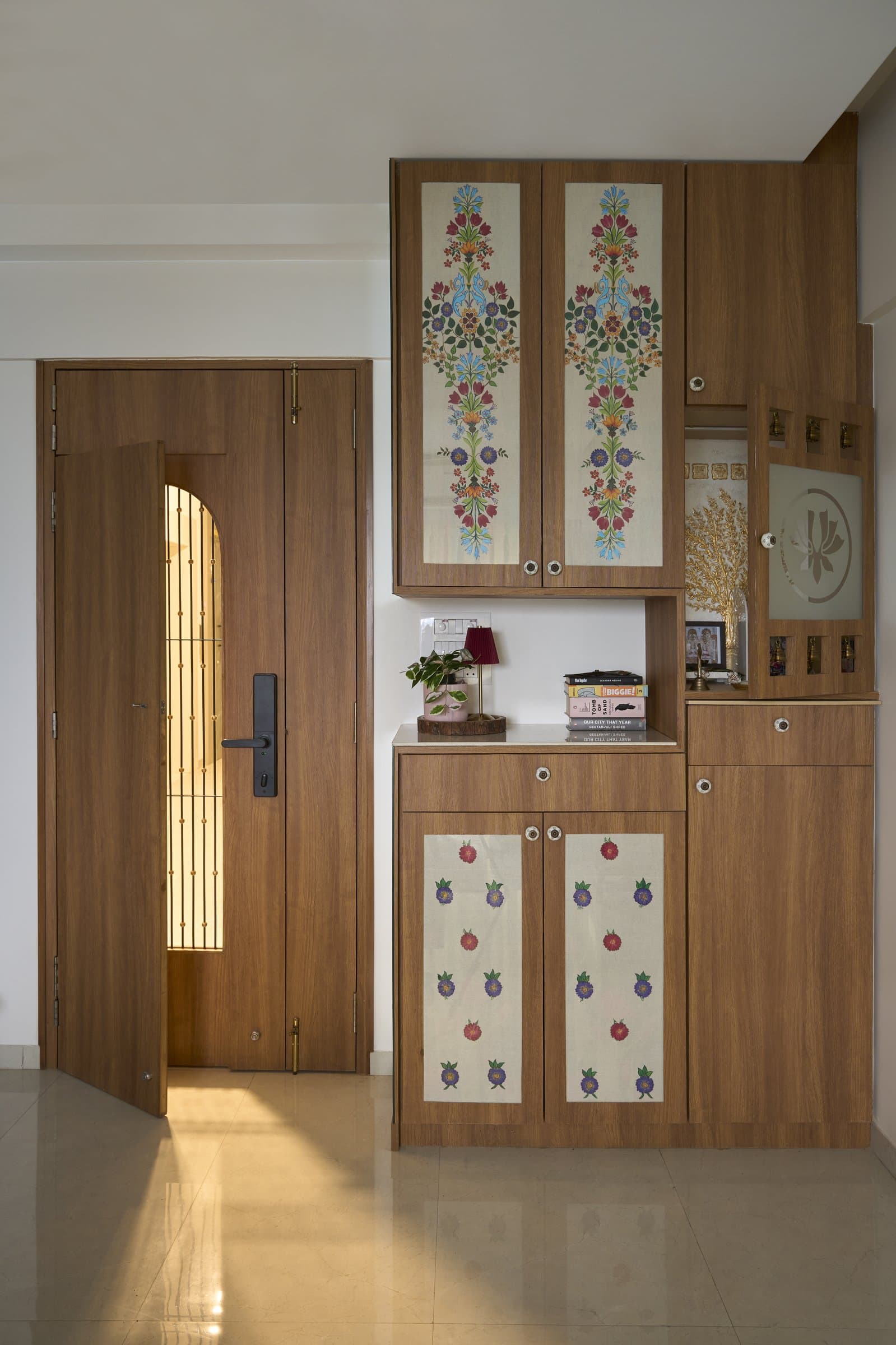 The entry foyer, where a walnut-toned cabinet with hand painted floral panels houses shoe storage and a small pooja niche in a single considered piece of joinery