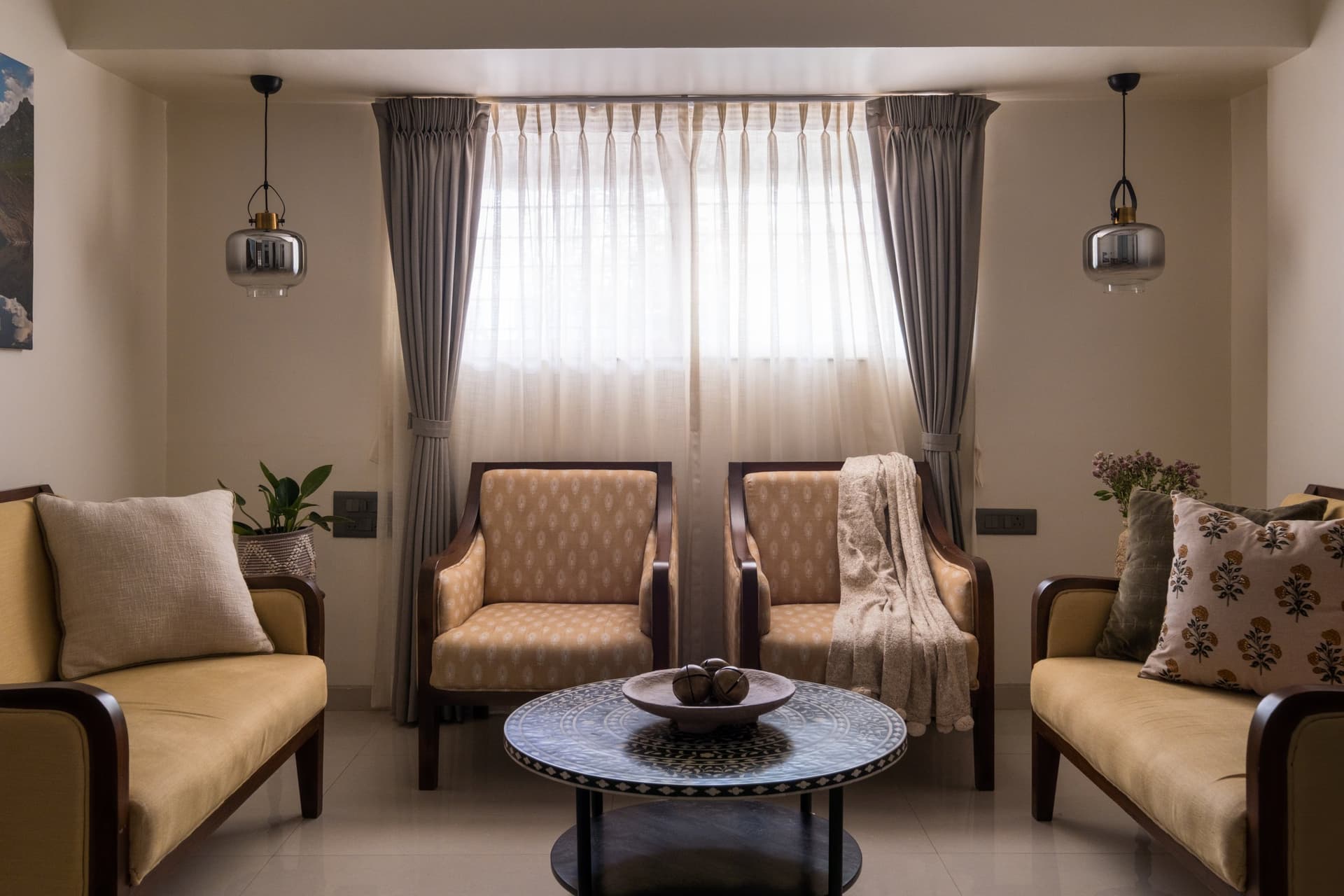 A secondary seating group in the living room, where sheer curtains and smoke-glass pendants lend balance to the composition