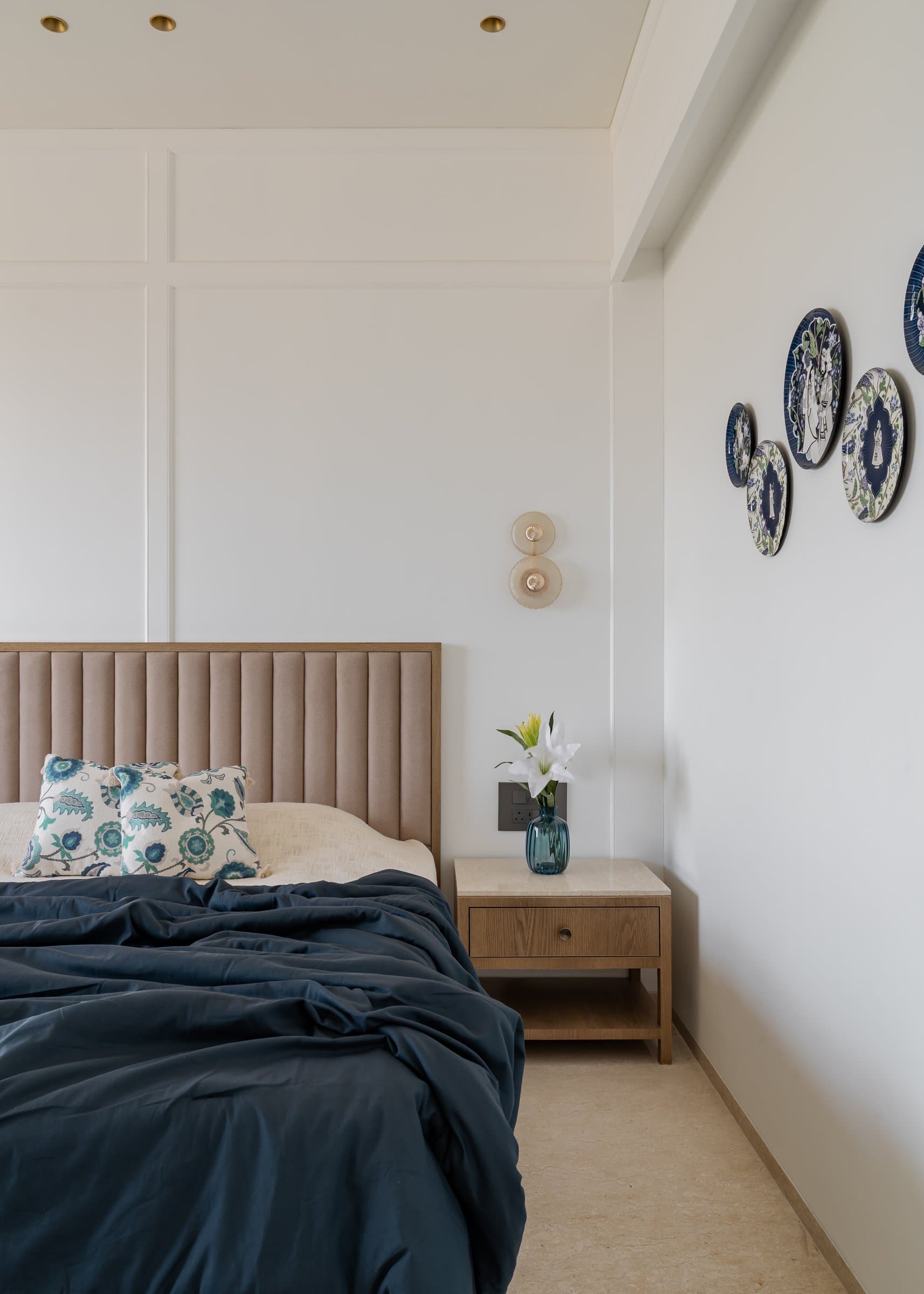 A cluster of blue-and-white decorative plates beside the bed, paired with a warm oak bedside table