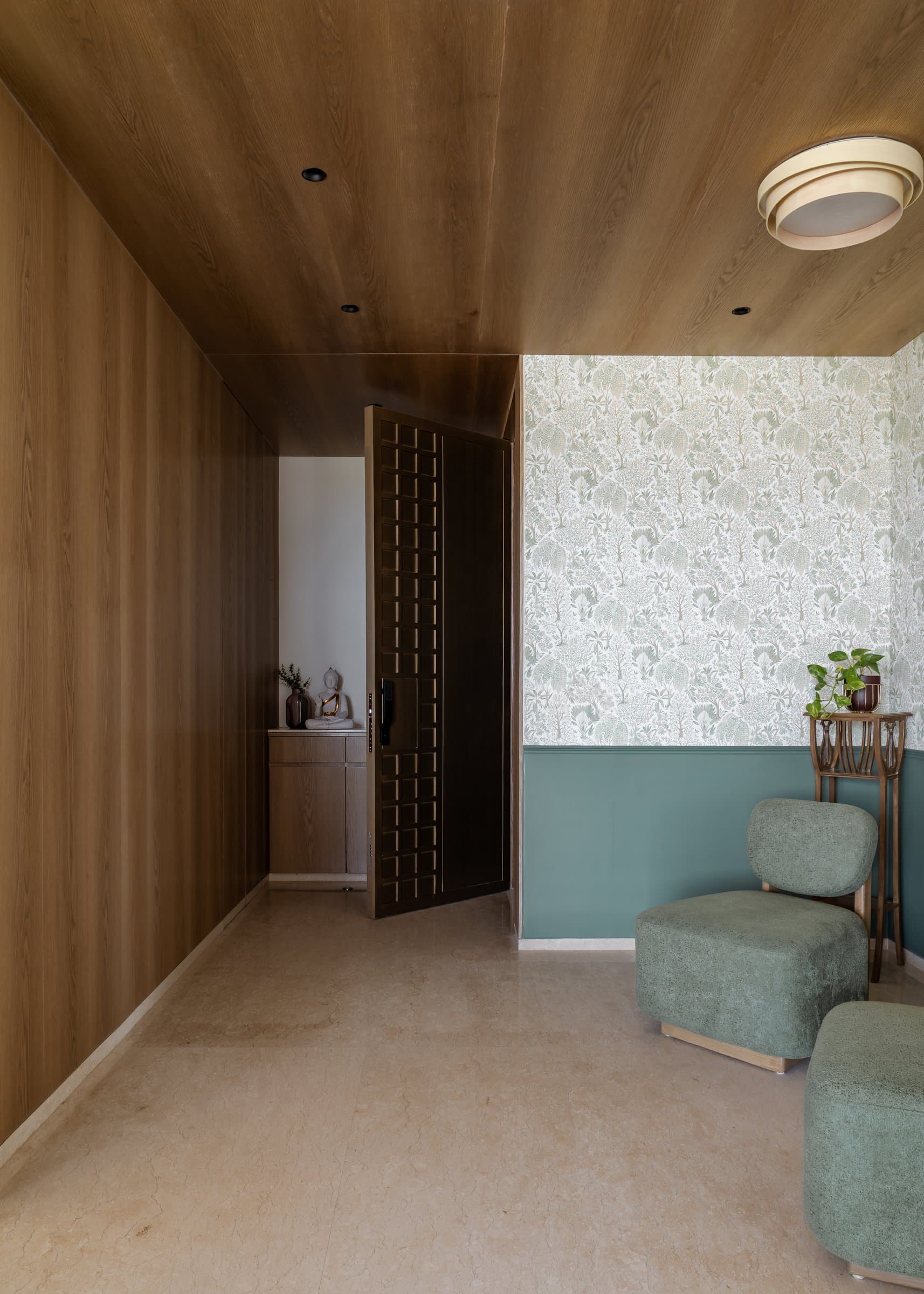 The foyer, where a ribbed oak ceiling meets a sage botanical wallpaper and a teal wainscoted dado