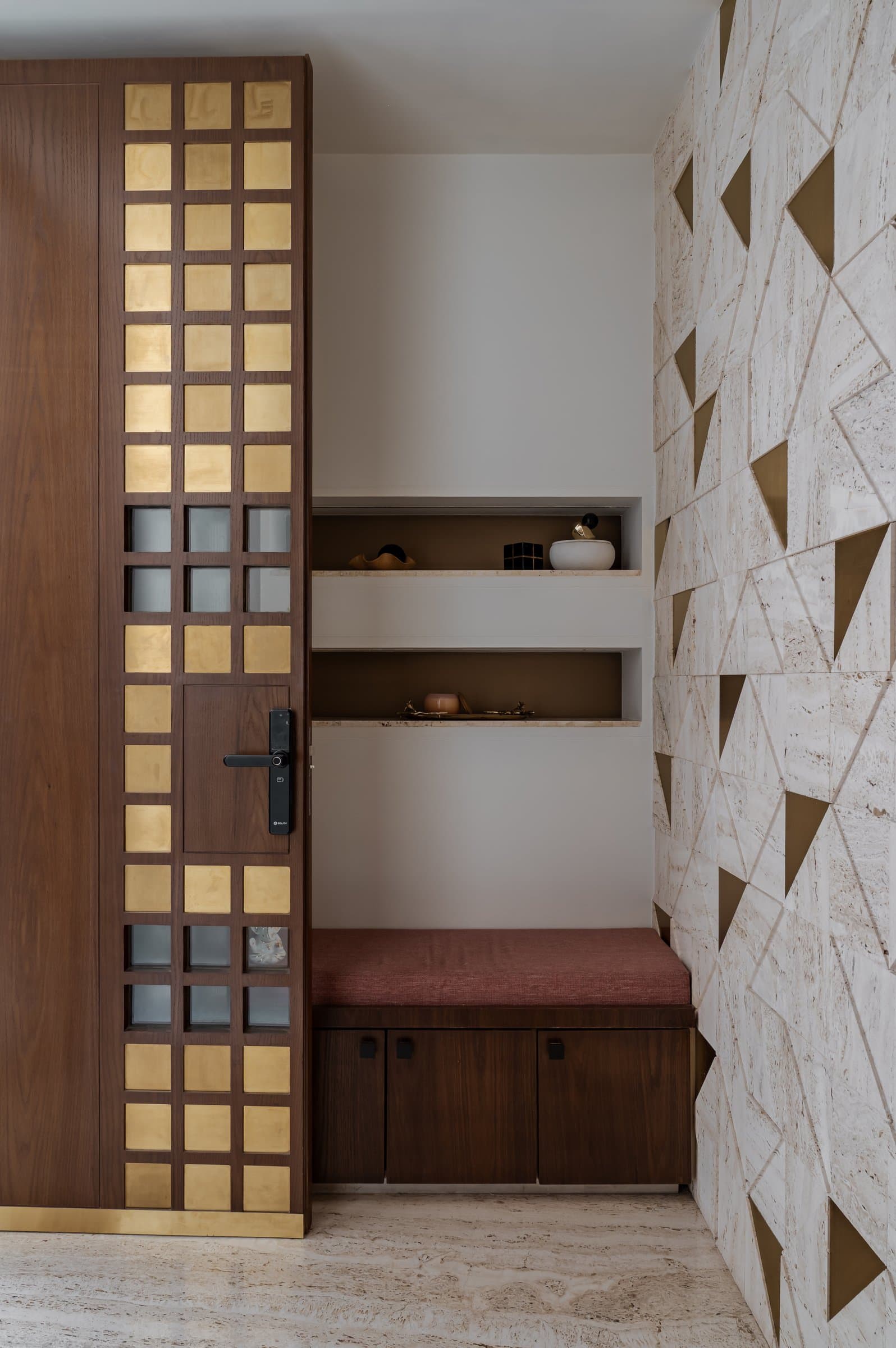 The vestibule, where a travertine wall with triangular brass inlays echoes the brass grid of the pivot door