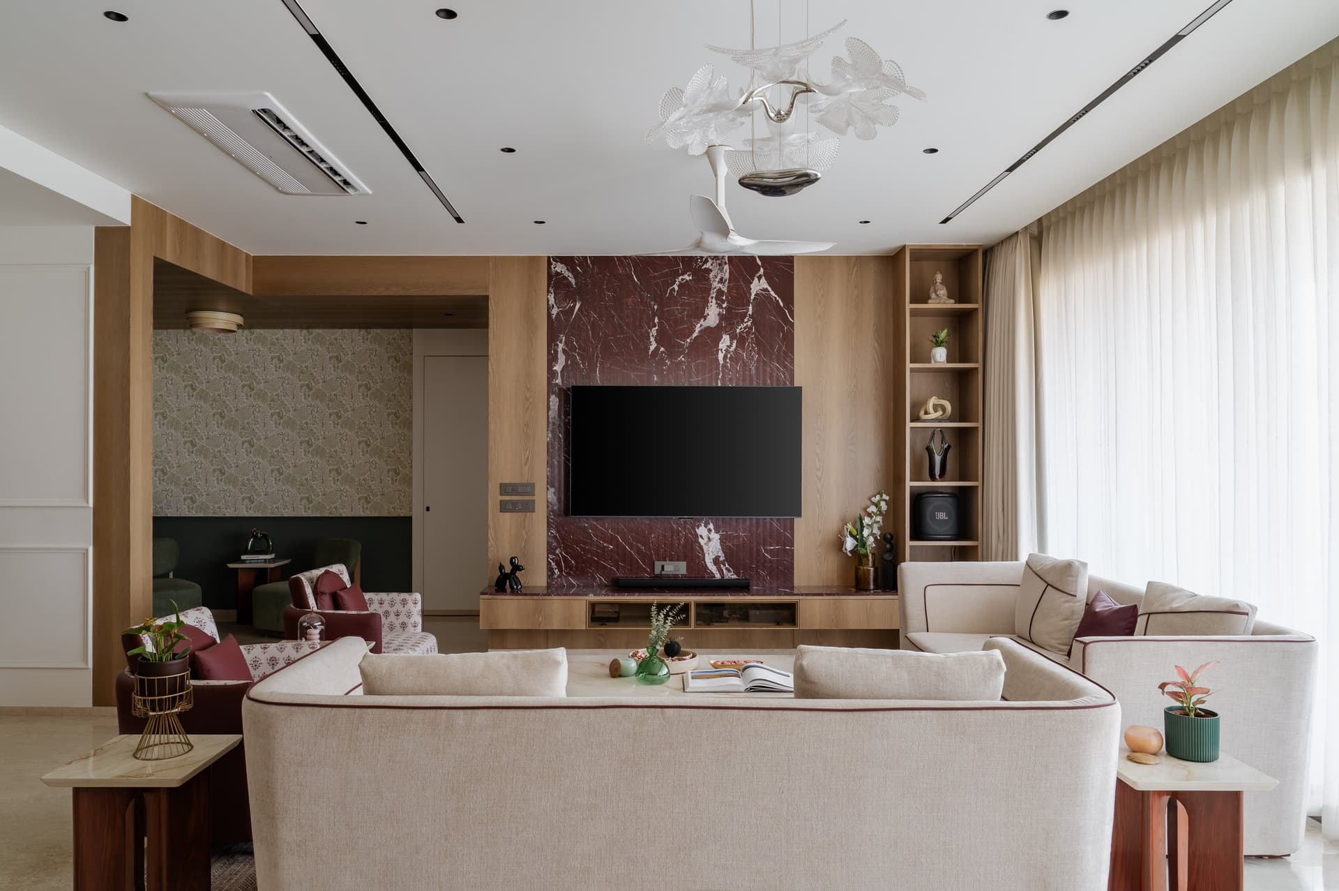 The living room, anchored by an oxblood marble media wall veined in white against warm oak panelling