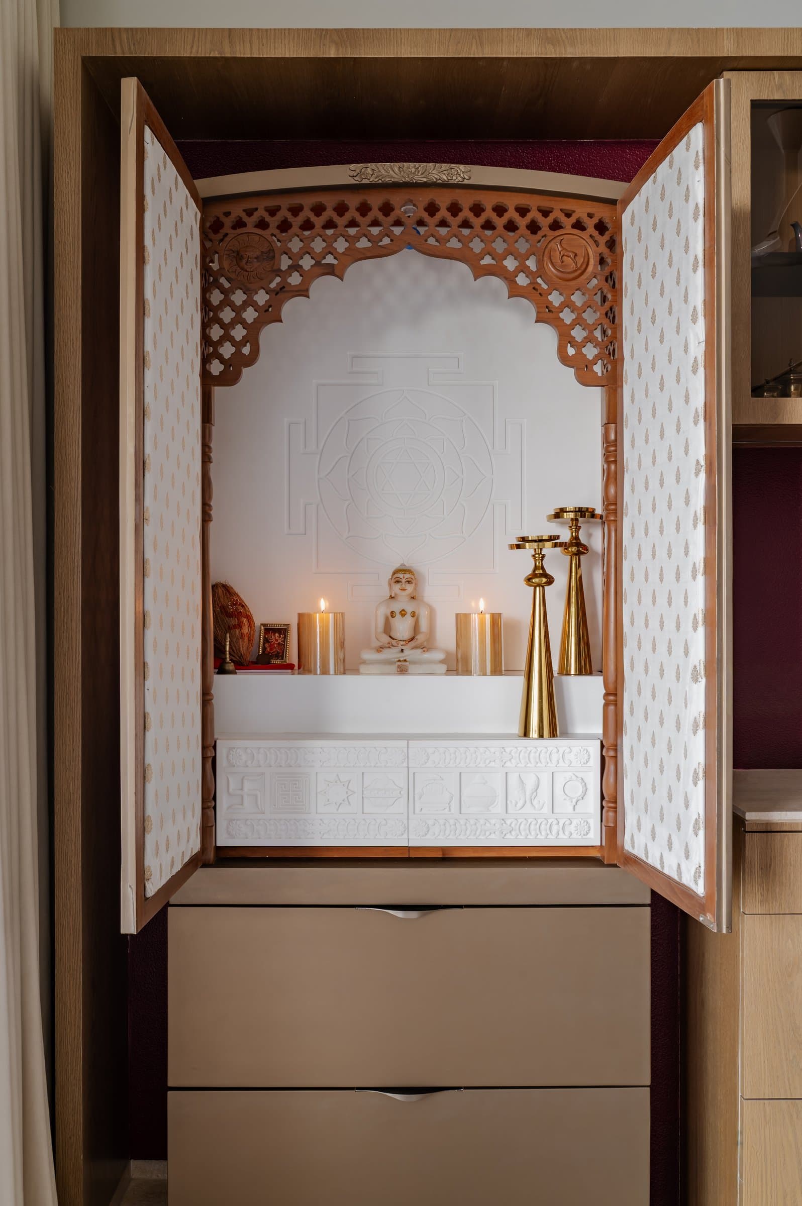 The pooja shrine, a carved timber jaali arch framing a marble idol against a wall etched with sacred geometry
