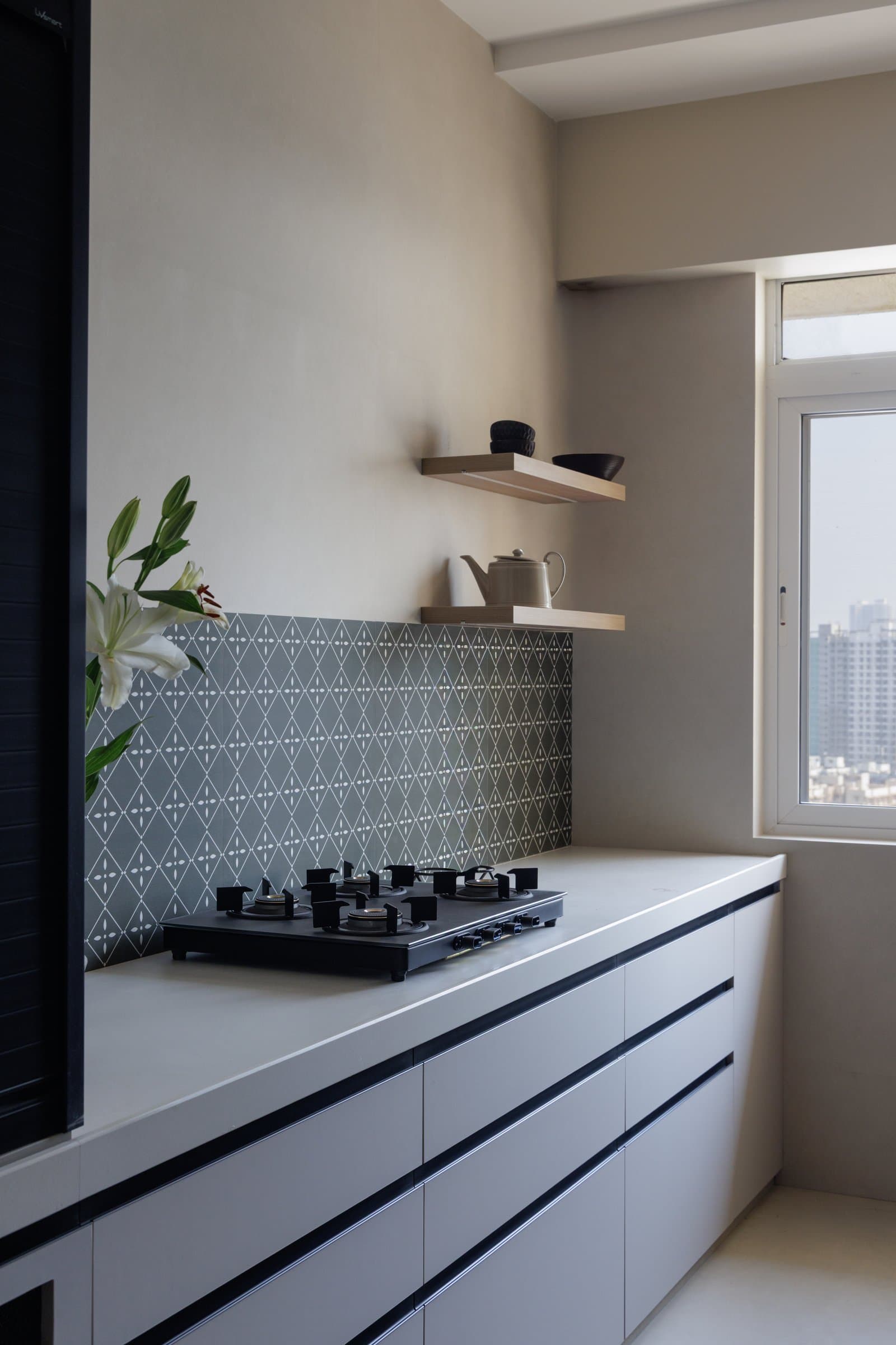 The galley kitchen, where handleless white cabinetry and a charcoal patterned backsplash meet pale wood open shelves