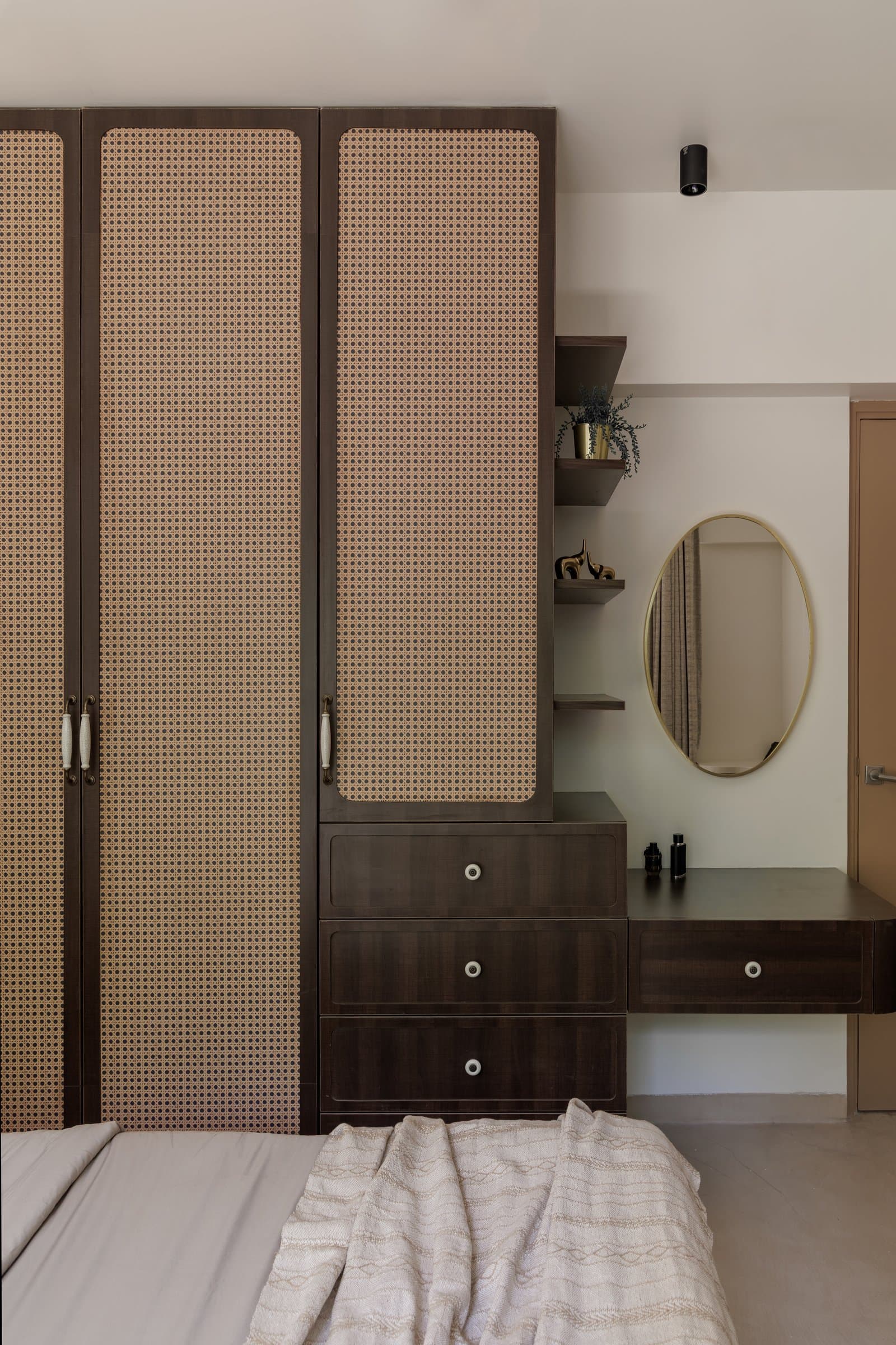 In the master bedroom, cane-fronted cabinet doors and a compact dressing counter introduce tactile depth without weight