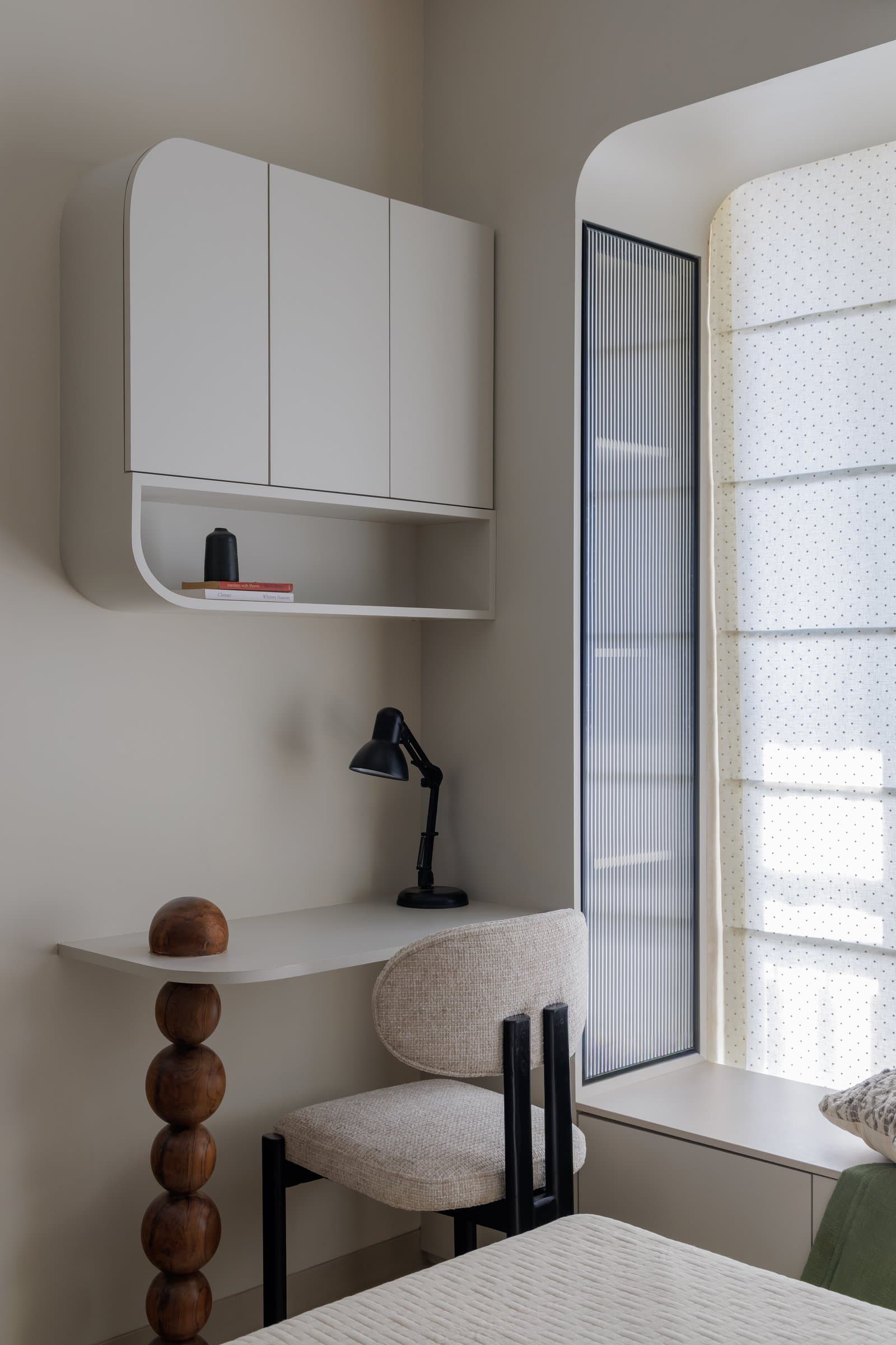 The study nook within the guest bedroom, its rounded storage unit and turned wooden pedestal echoing the dining table's silhouette