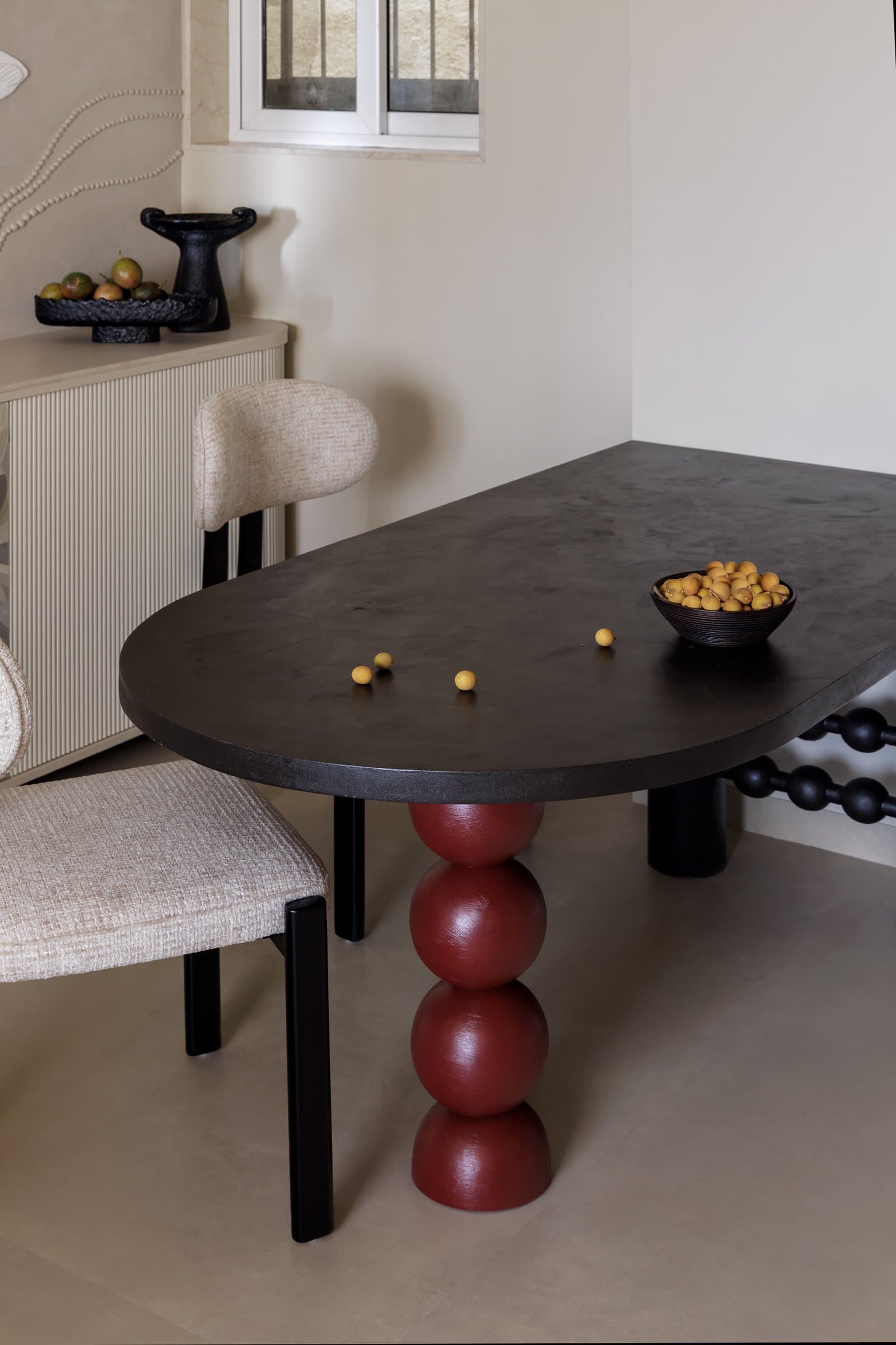 A closer view of the dining table, its blackened top resting on sculpted oxblood spheres against fluted cream joinery