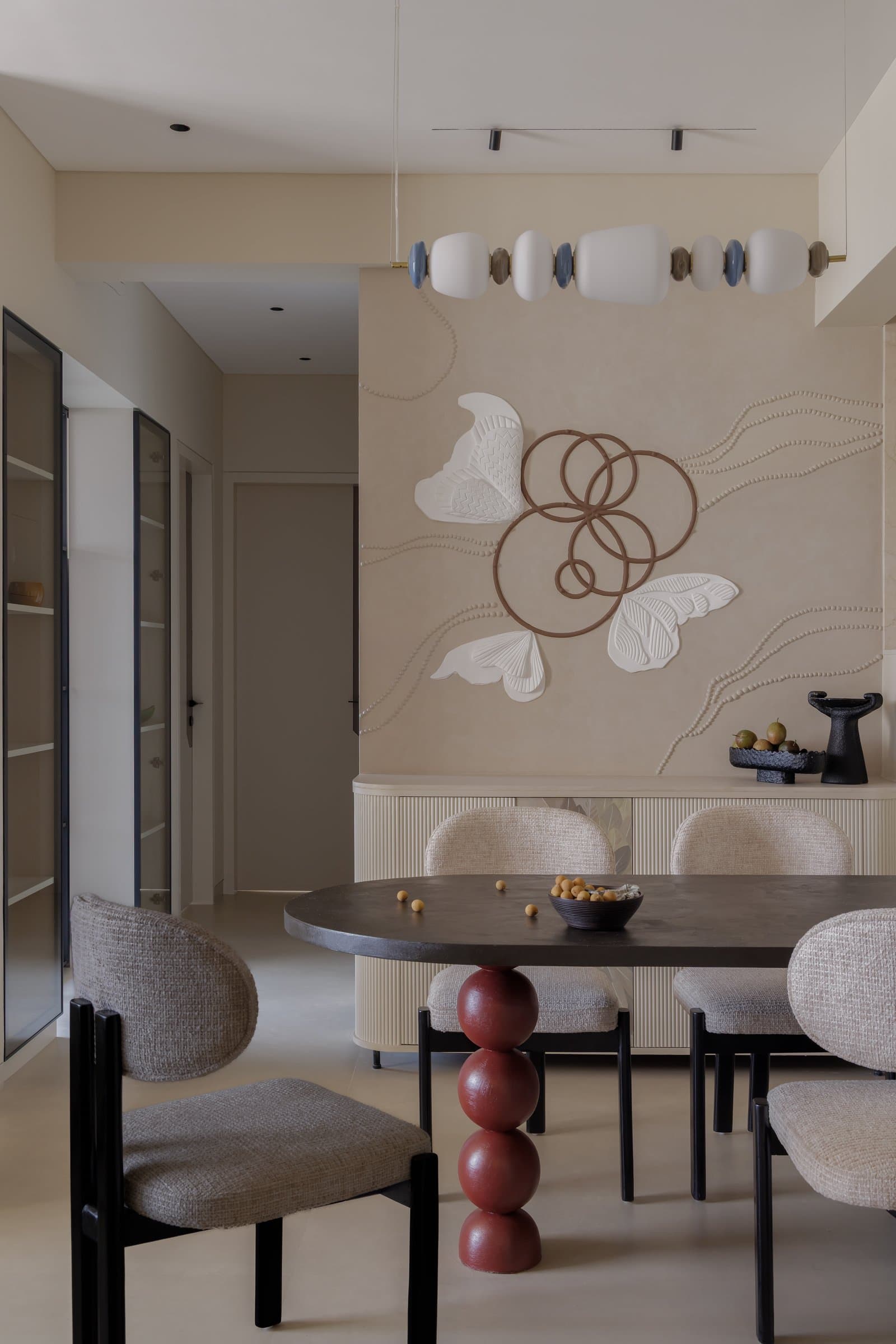 The dining area, where an oval table on a stacked oxblood pedestal sits beneath a beaded relief mural of butterflies and copper rings