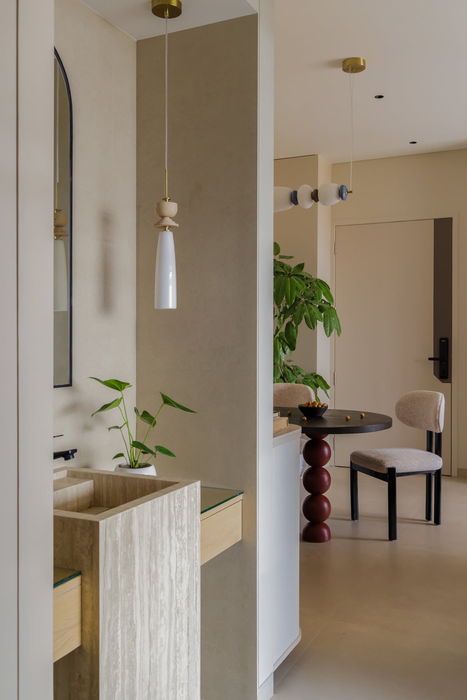 The powder room, where a travertine pedestal basin and slender pendant frame a glimpse back toward the dining area