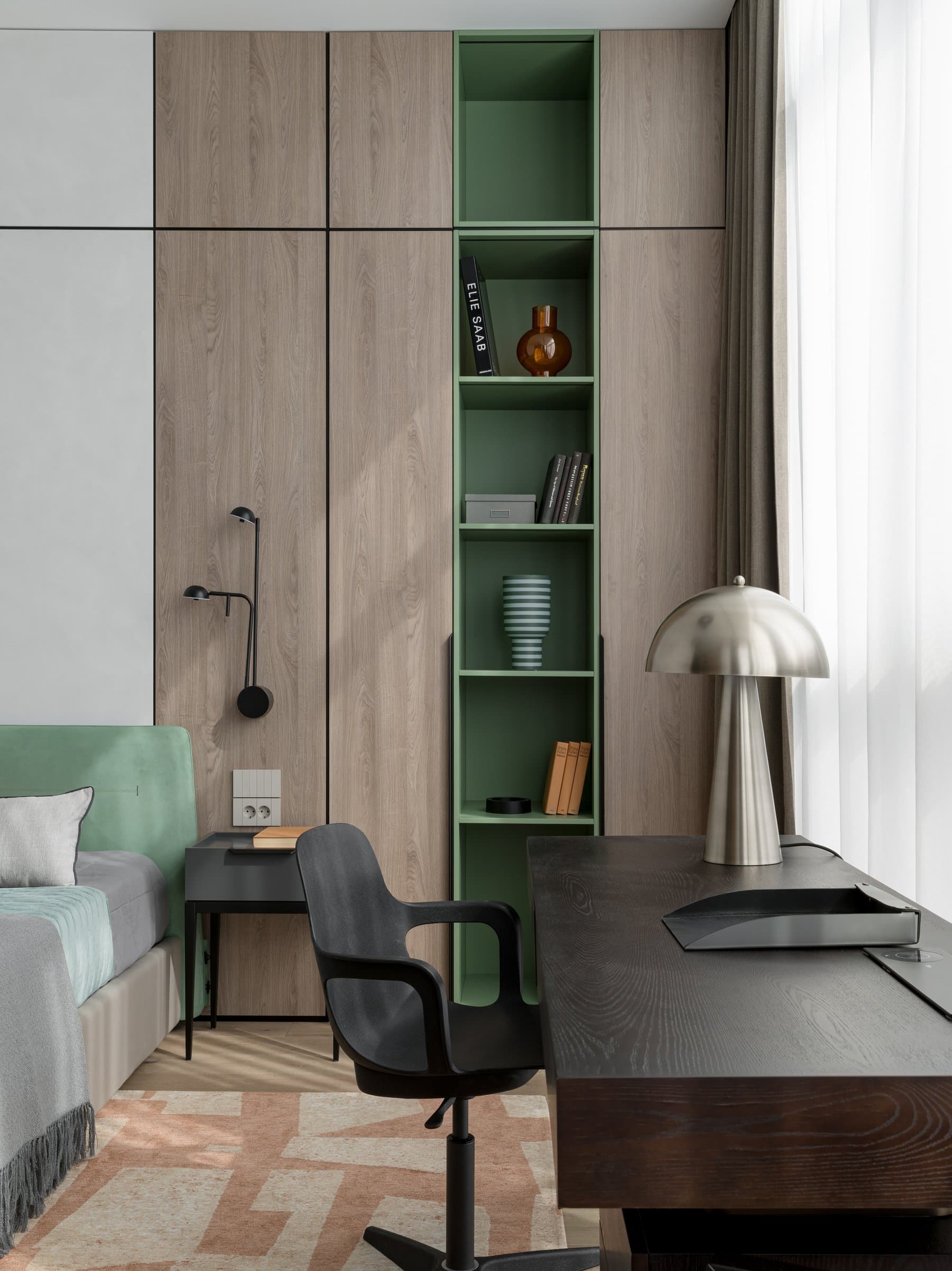 The compact workspace beside the bed, with a dark stained desk, sculptural task chair, and green-lined open shelving