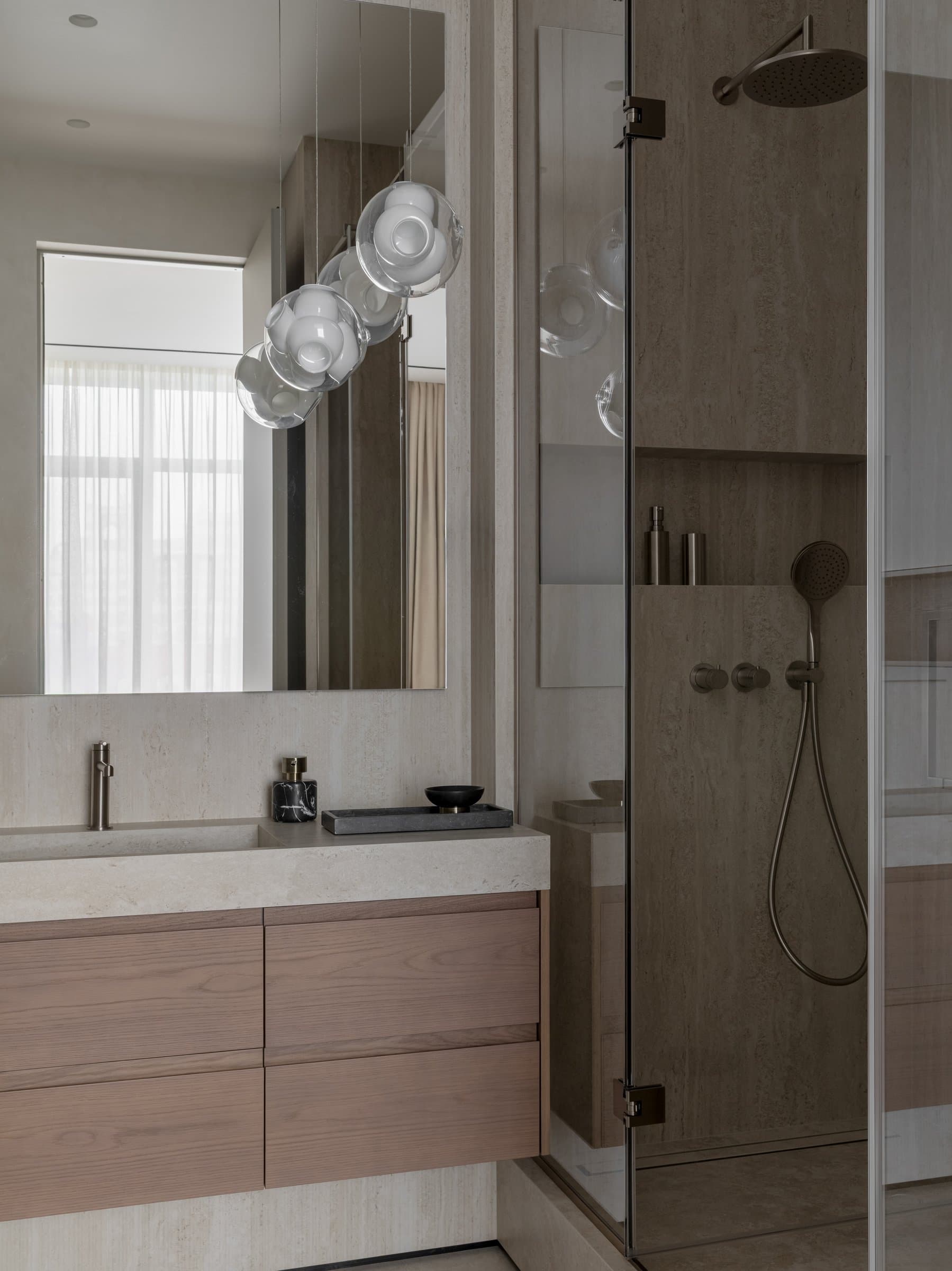 The shower zone, where stone-clad walls and brushed fittings continue the vanity's material vocabulary