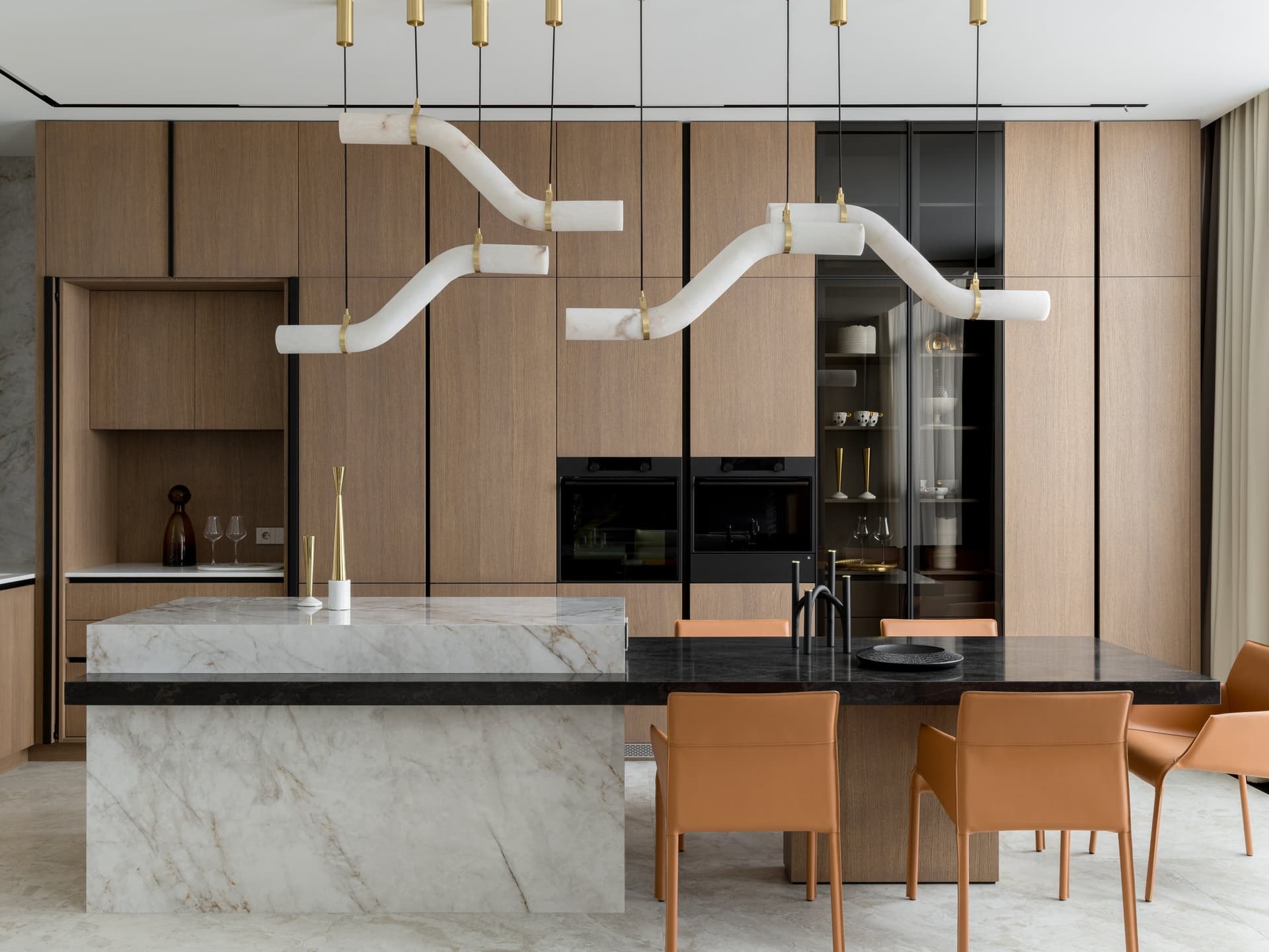 The kitchen and dining zone, where a monumental stone-veined island meets tan leather chairs beneath a segmented stone pendant