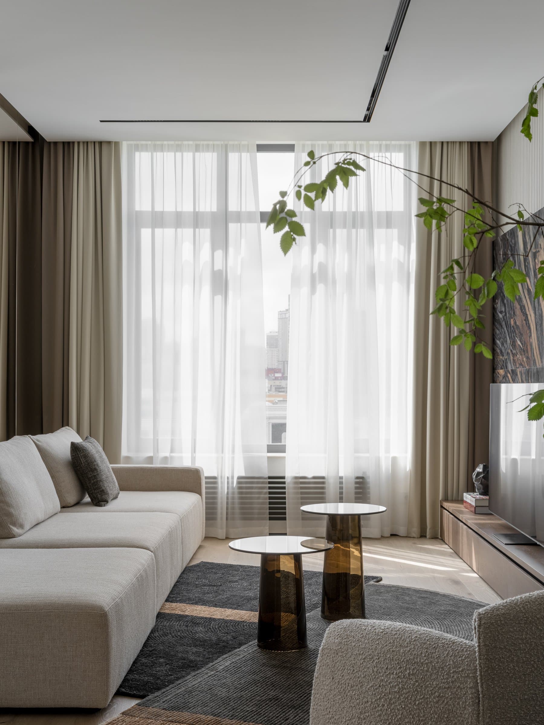 The seating side of the living room, where sheer drapery softens the panoramic glazing to a diffused wash of light