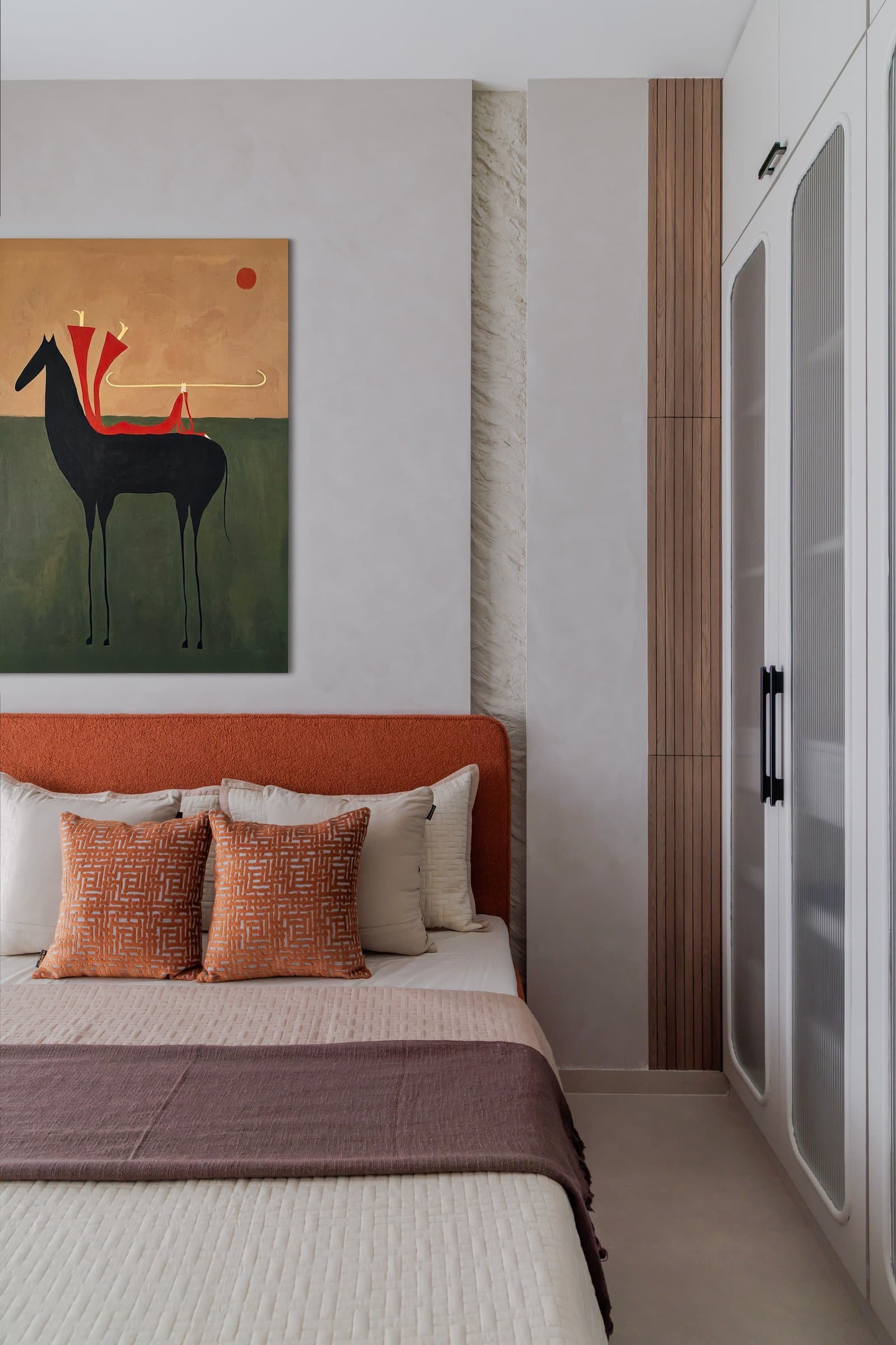 The guest bedroom, where a rust bouclé headboard and a painting of a black horse establish the room's warmer palette