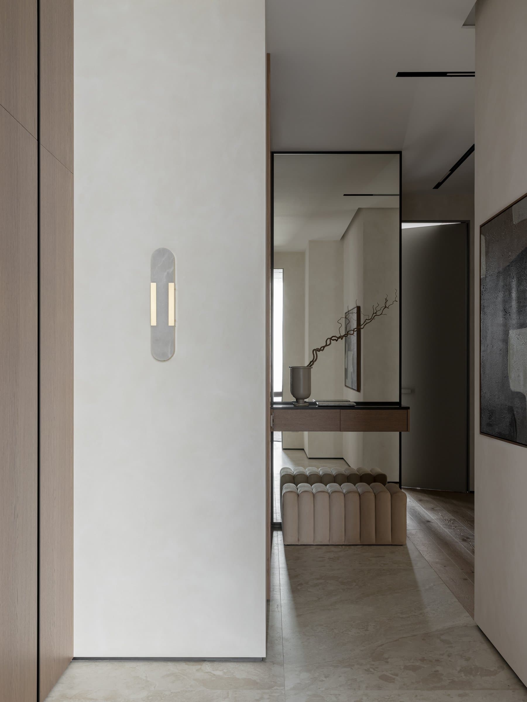 The entry, where a channel-tufted bench and full-height mirror extend the volume against soft plaster walls
