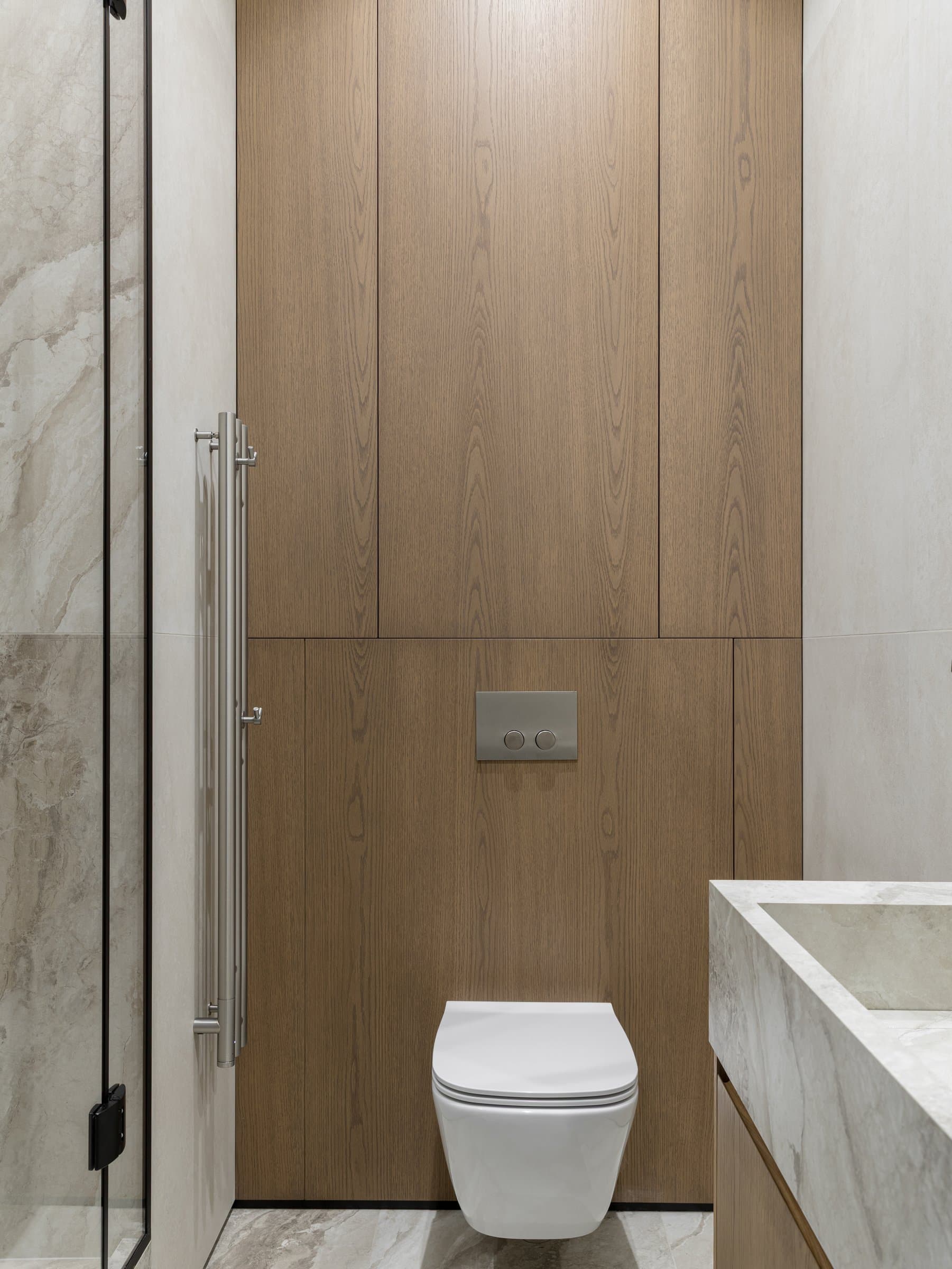 The guest bathroom, where a panel of warm oak carries the fixtures against stone-toned surfaces