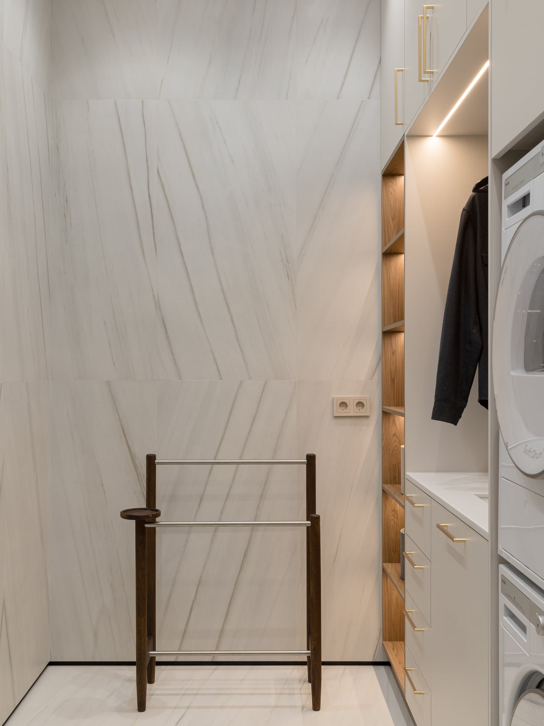 The laundry room, where white-veined stone meets pale cabinetry and a slender wooden valet stand