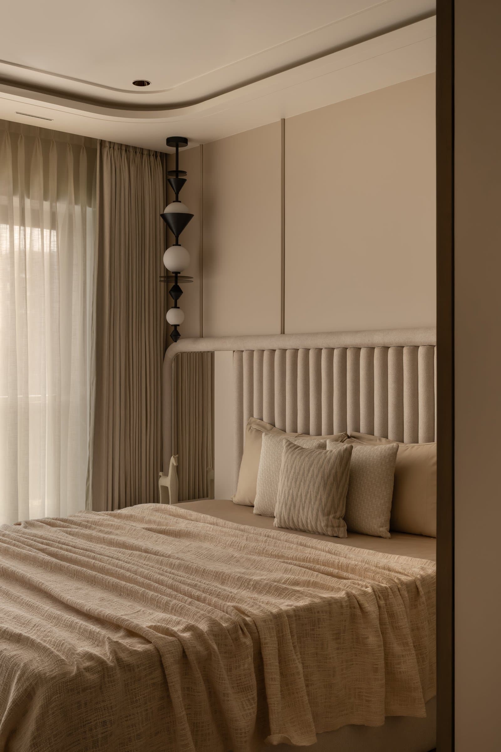 The guest bedroom, where a fluted upholstered headboard and a vertical composite pendant establish a quieter register