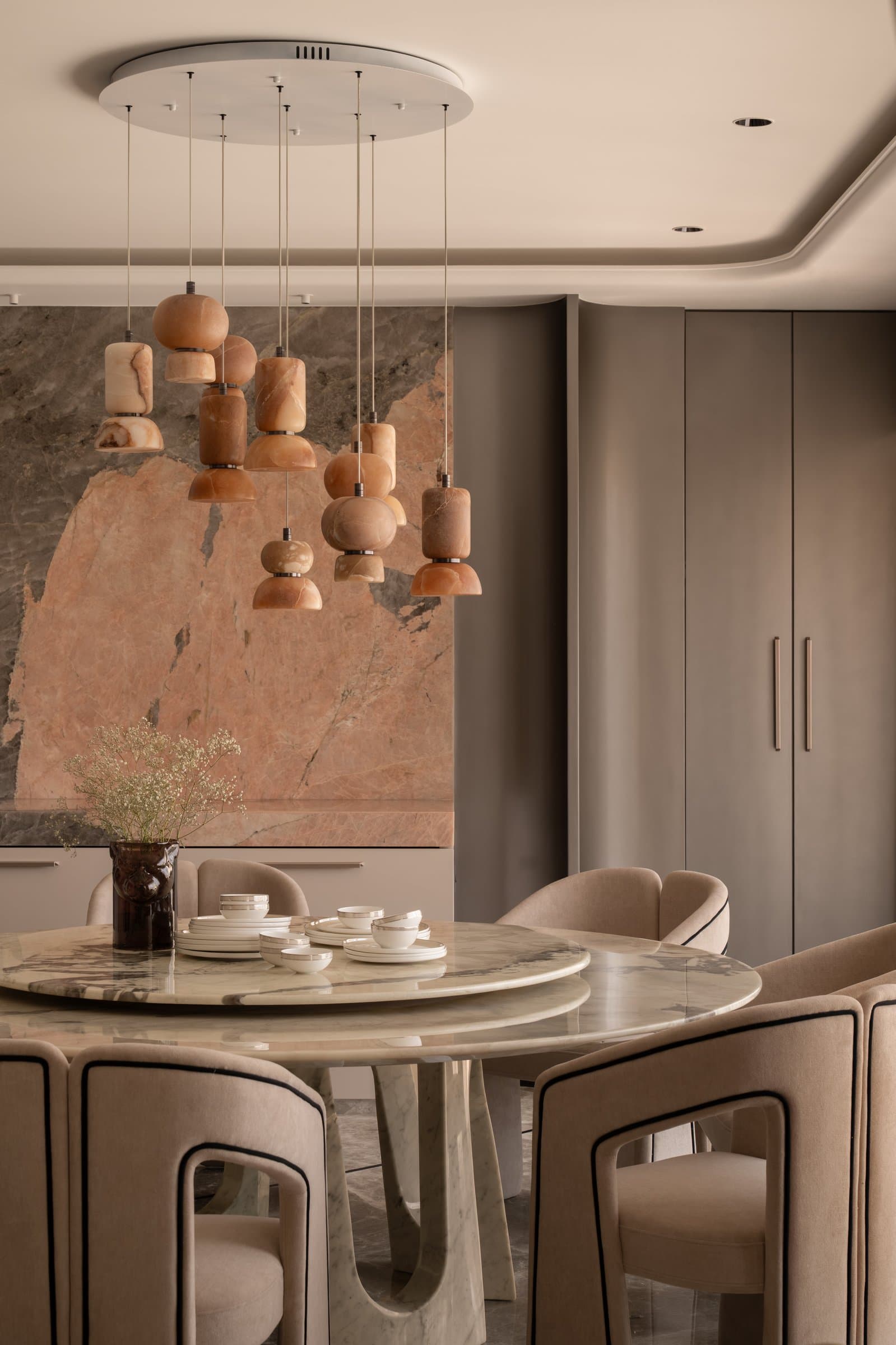 The dining table, where a sculptural marble base and stacked stone pendants reinforce the room's material argument