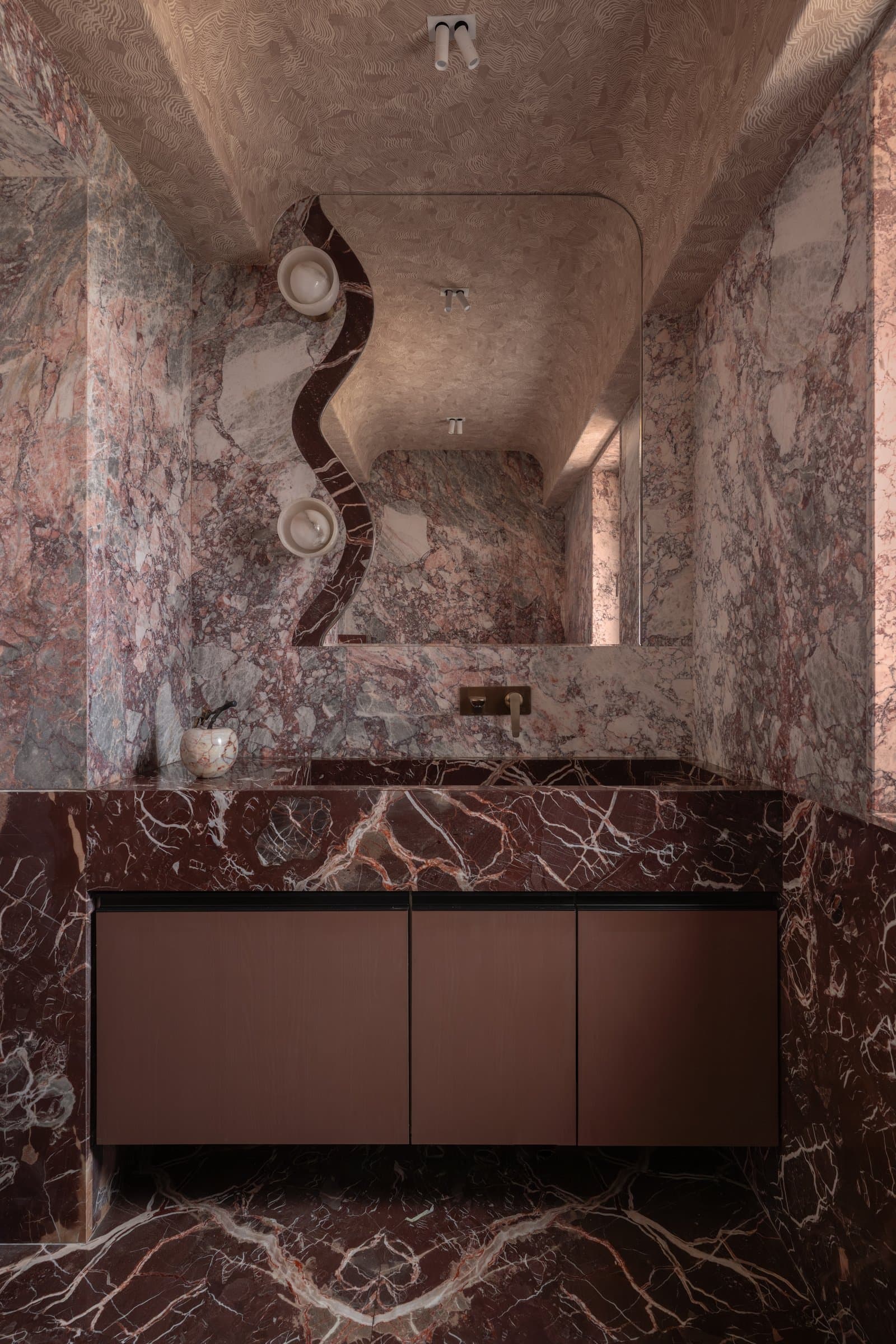 The powder room, where richly veined burgundy marble creates a cavernous, immersive volume