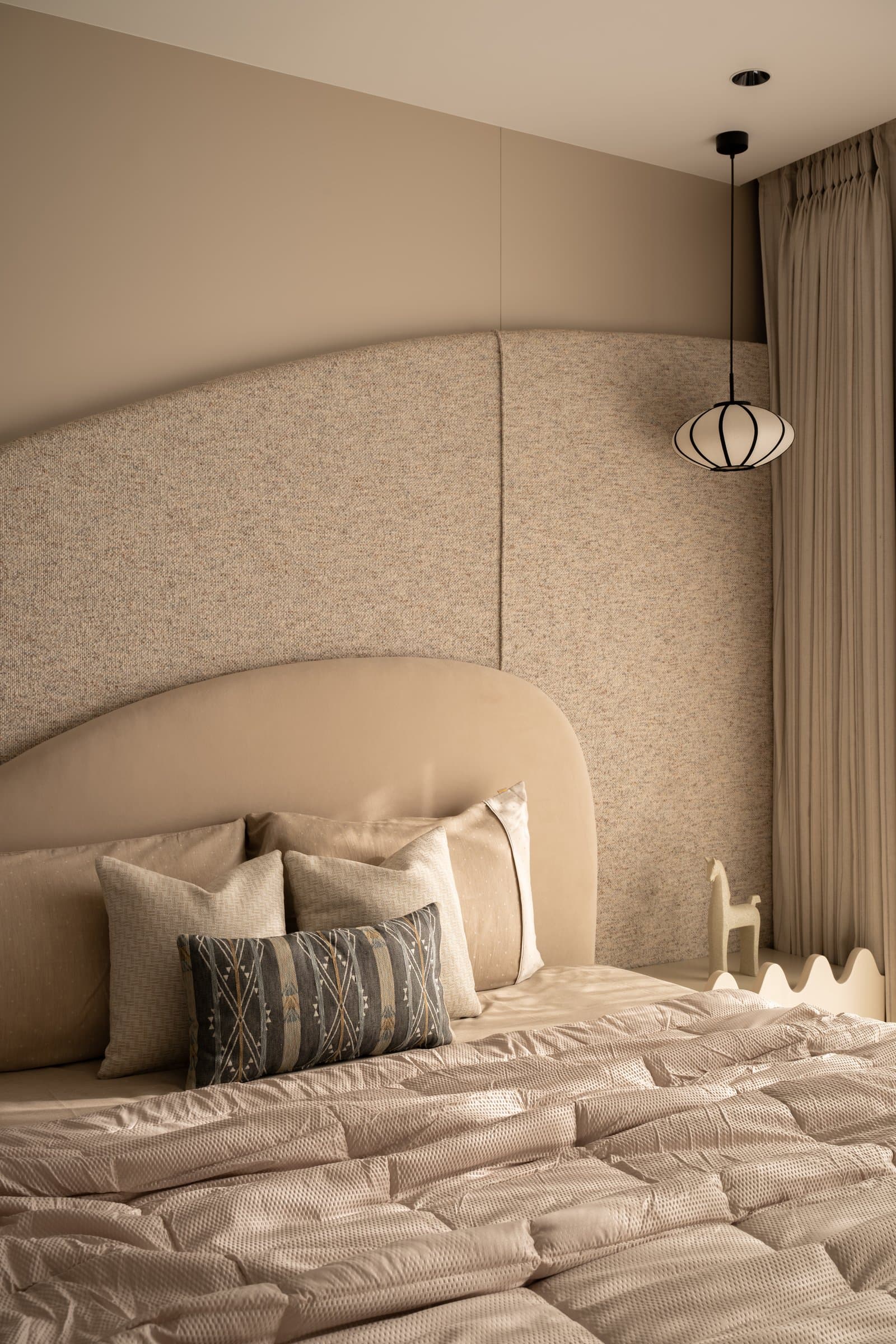 The second bedroom, where an arched upholstered headboard meets a textured wall panel and a lantern pendant