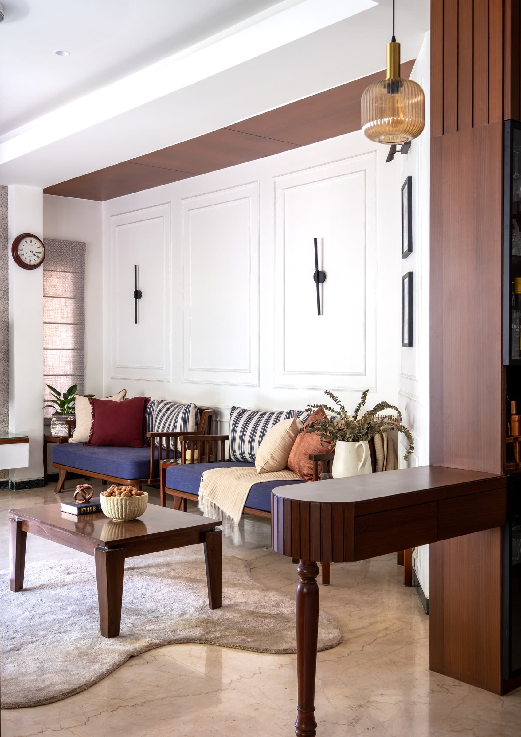 A pair of wooden daybeds with blue cushions set against a panelled wall, softened by a warm ribbed glass pendant