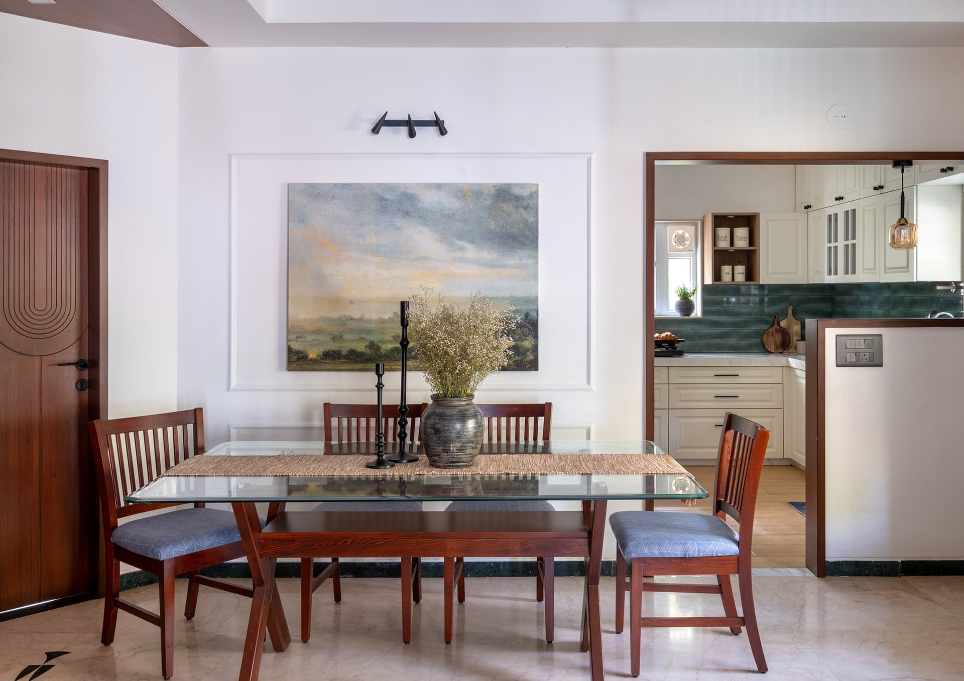The dining area, defined by a framed landscape painting and a broad opening into the kitchen