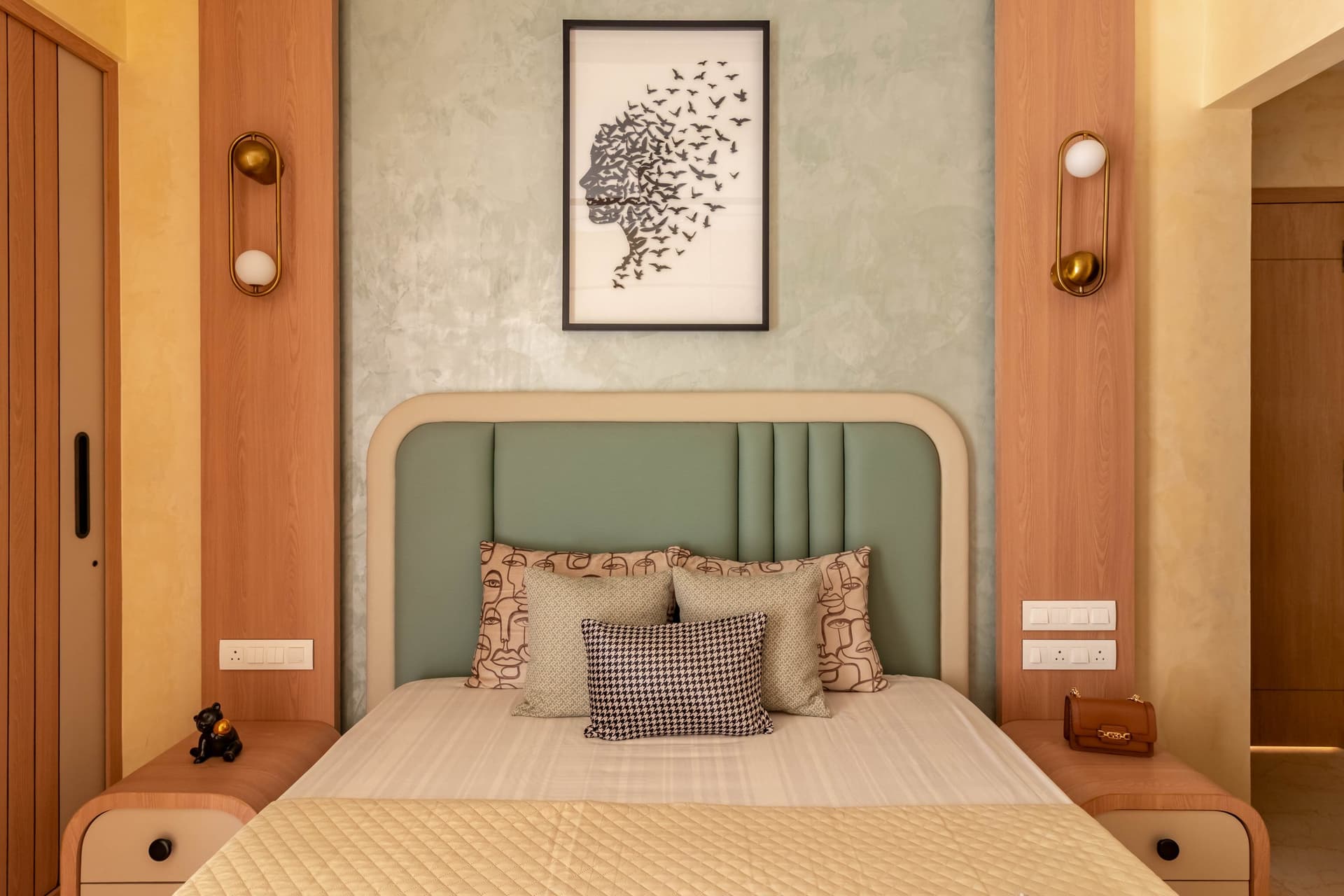 The principal bedroom, where a sage upholstered headboard and brass-and-globe sconces establish a cooler, contemplative palette