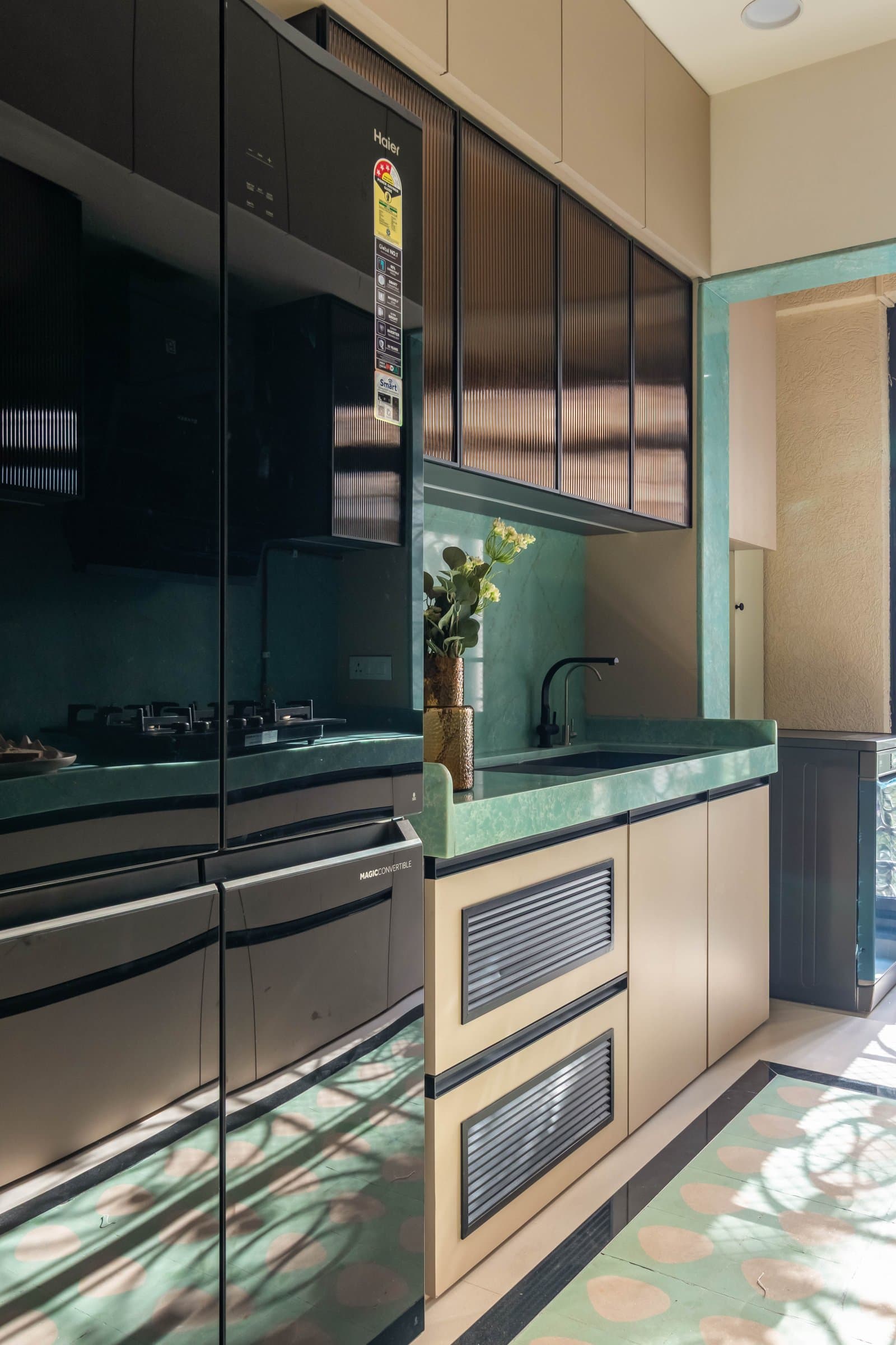 The kitchen's second run, with the green stone wrapping the sink and a dark-glass appliance cabinet absorbing the harder-working elements