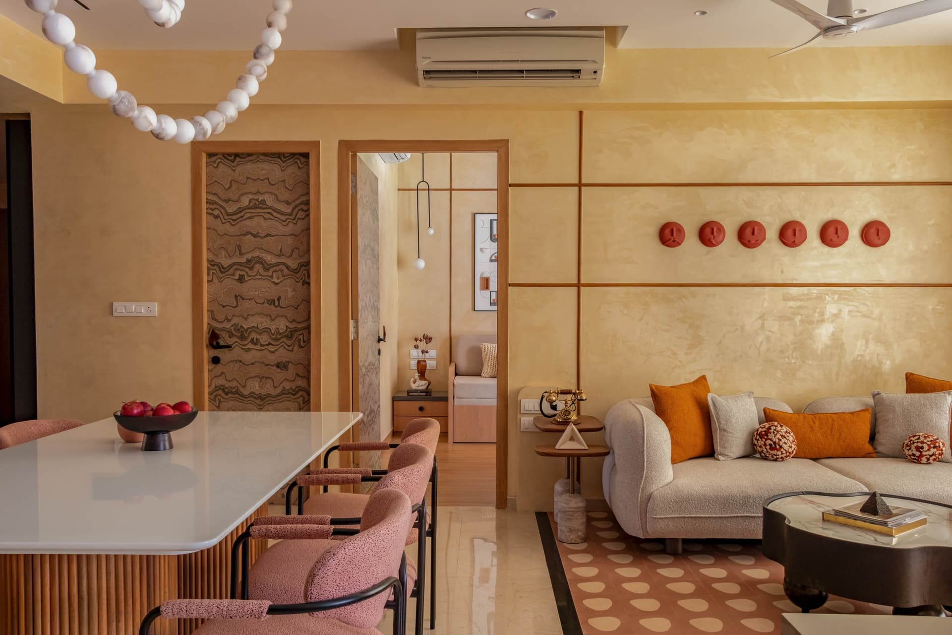 Looking back from the dining zone, terracotta face-plaques thread across the limewashed wall above the living-room sofa