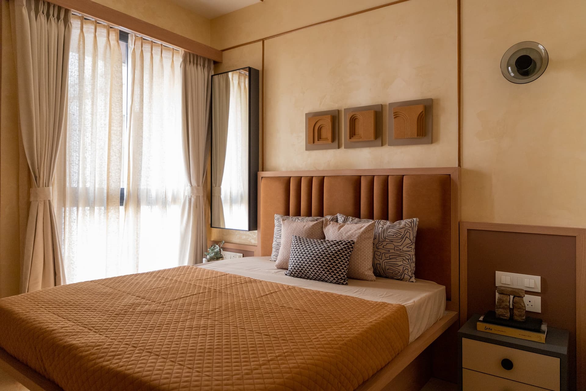 The second bedroom, its channelled rust-toned headboard set beneath a triptych of moulded arch reliefs