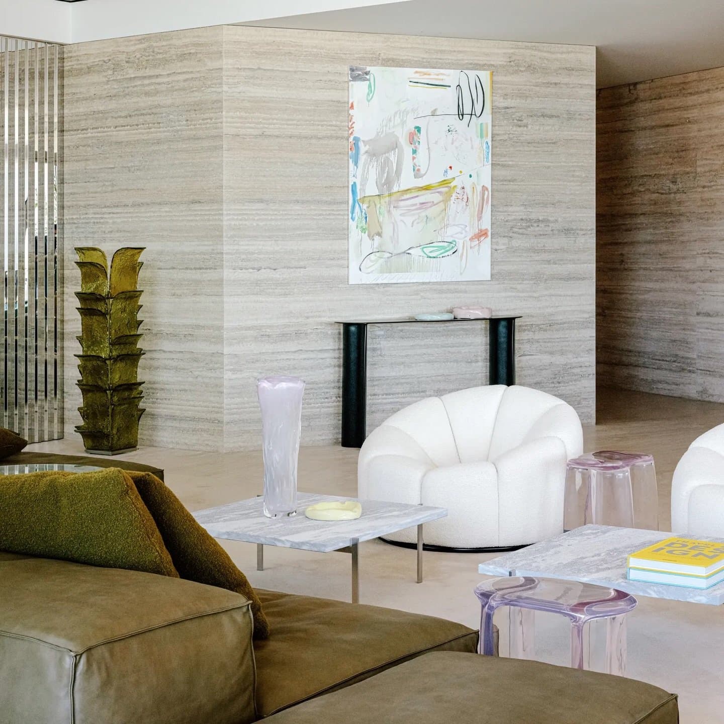 A travertine-clad wall carries the room's texture, paired with a bouclé armchair and marble-topped tables.
