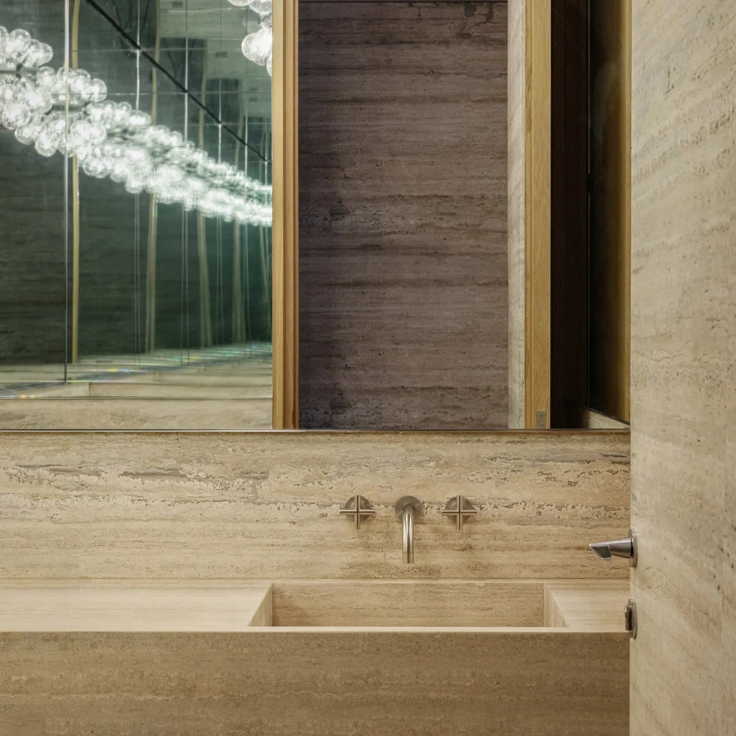 In the bathroom, a travertine vanity carries the composition through veining and soft directional light.