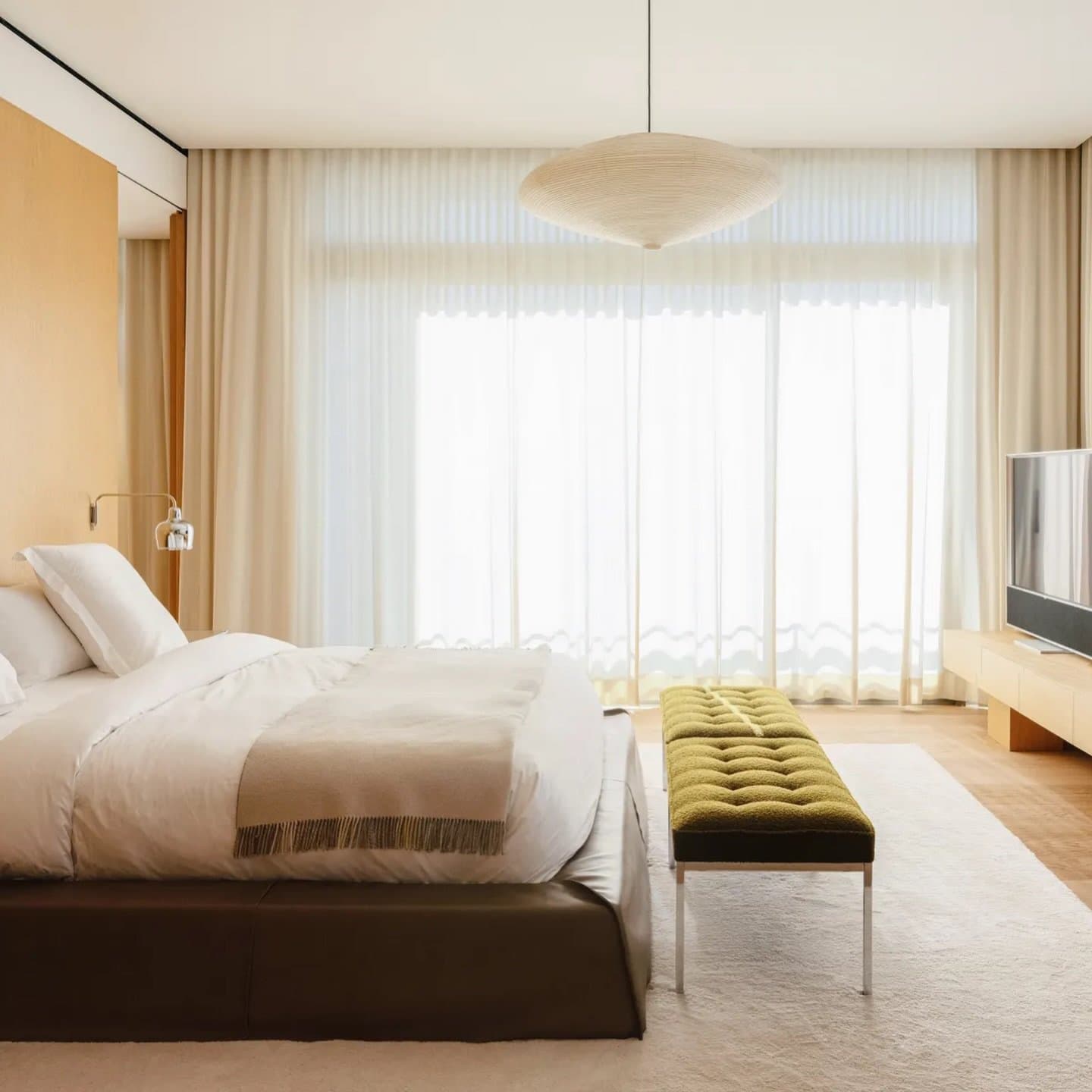 The master suite, wrapped in pale French oak, holds an olive tufted bench as its single strong colour note.
